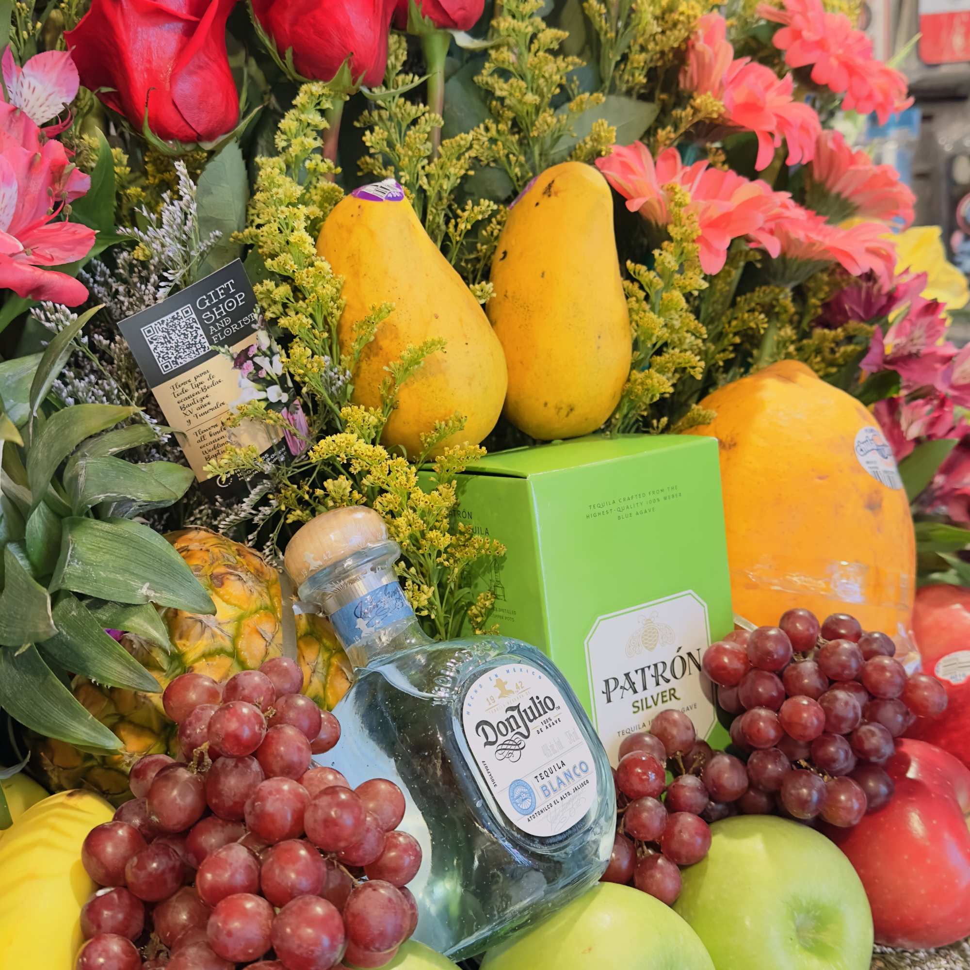 Fruit and flower arrangement with red roses, sunflowers, grapes, apples, and liquor bottles