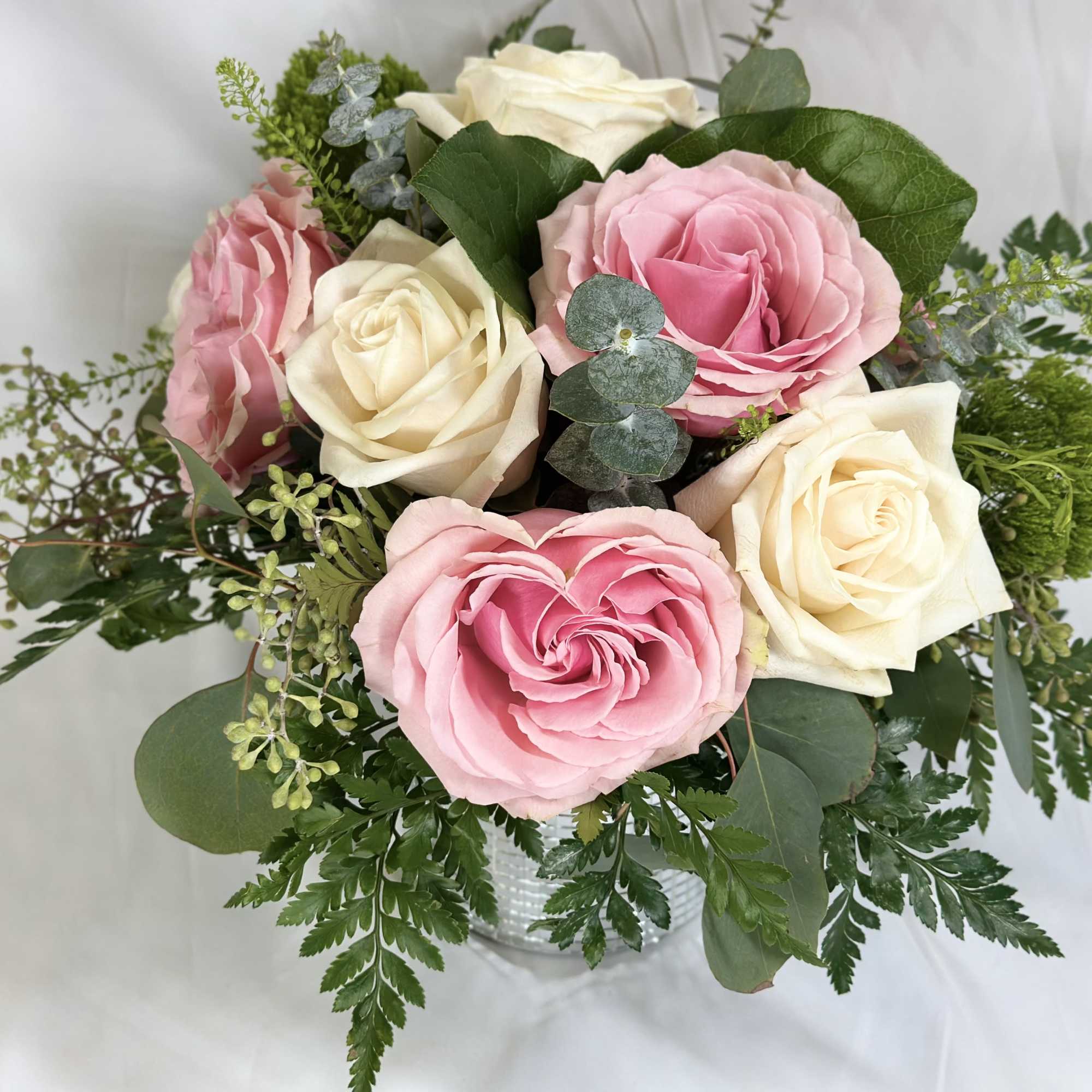 Pink and white roses arranged in a clear vase with greenery