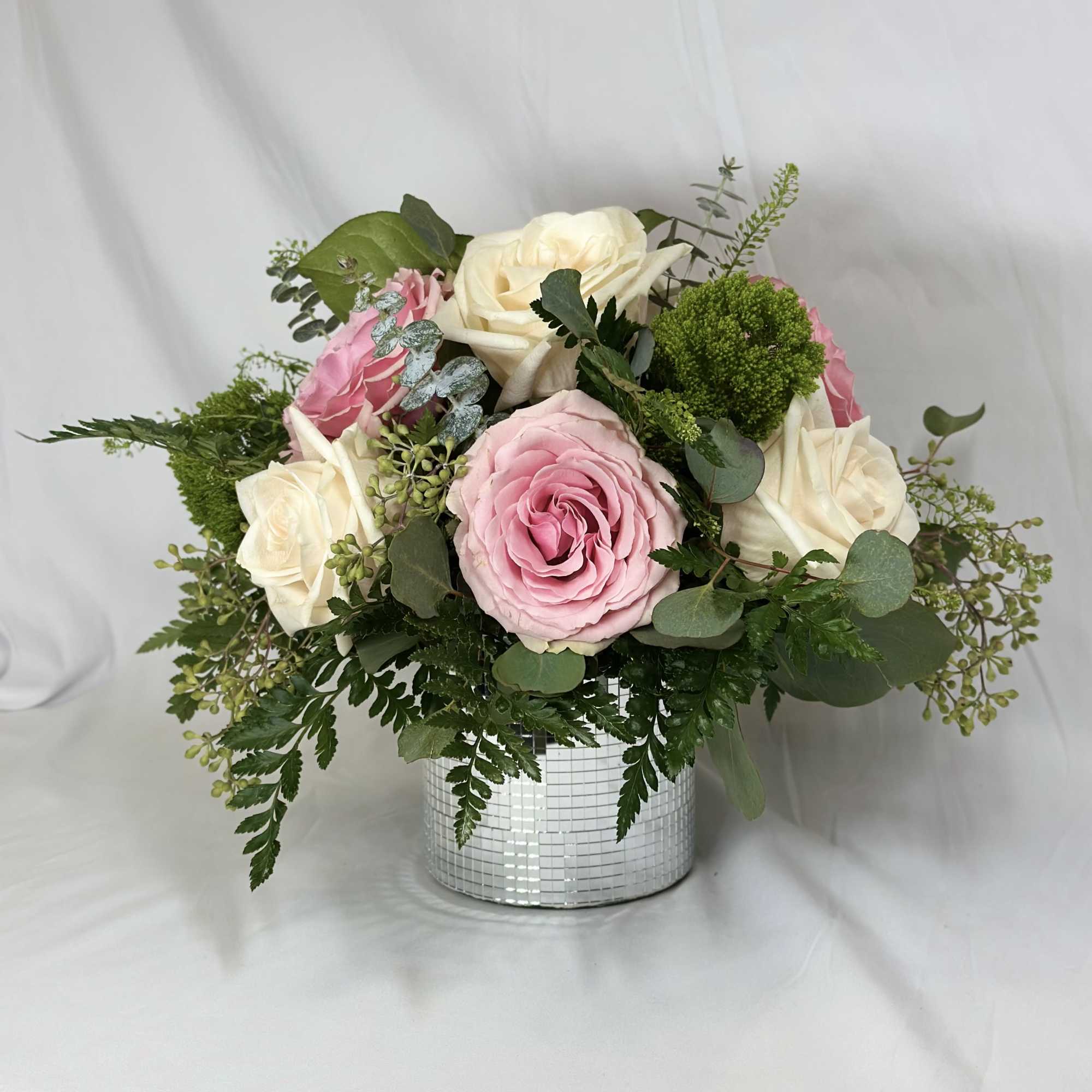 Pink and white roses arranged in a mirrored vase
