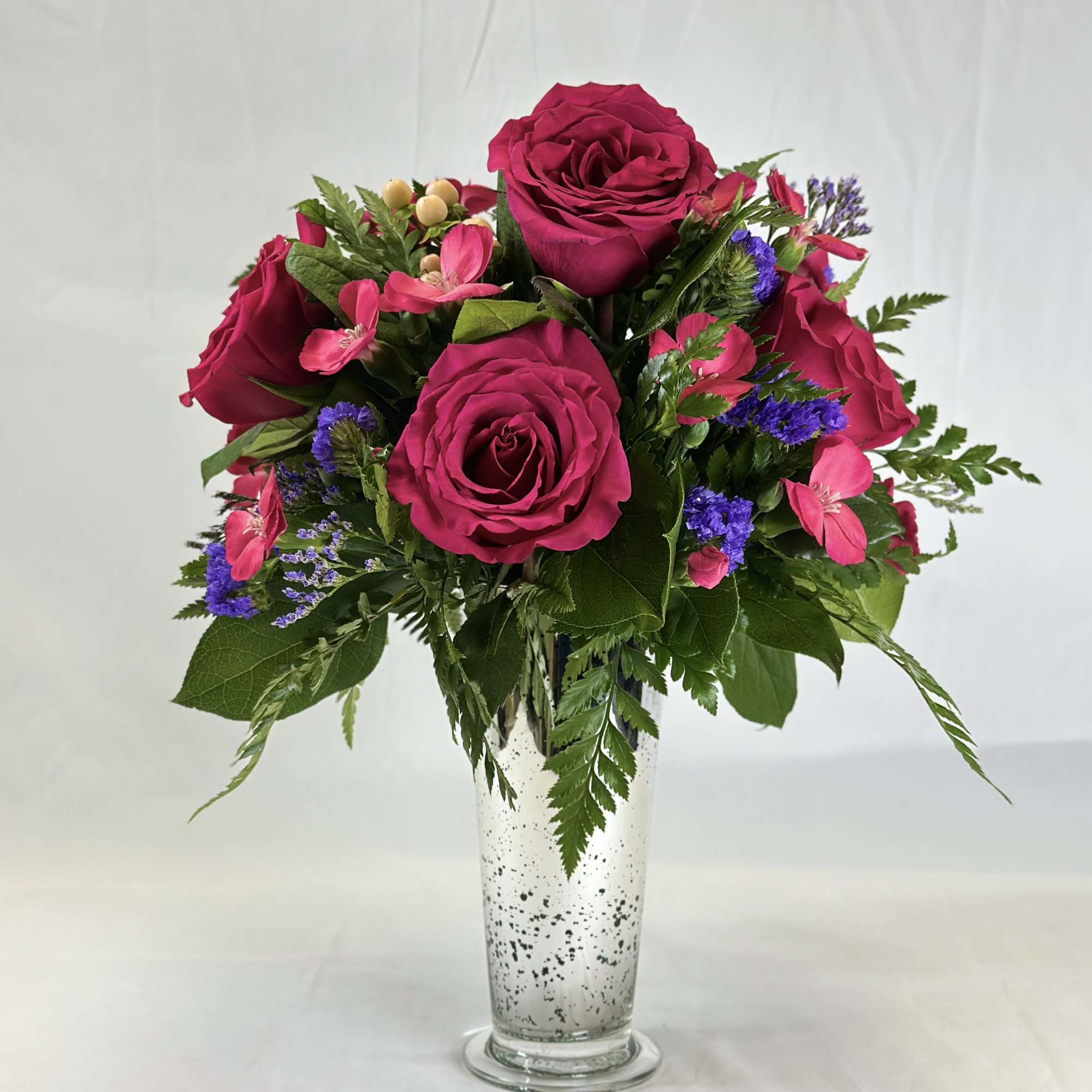 Bouquet of magenta roses and pink accents in a clear glass vase