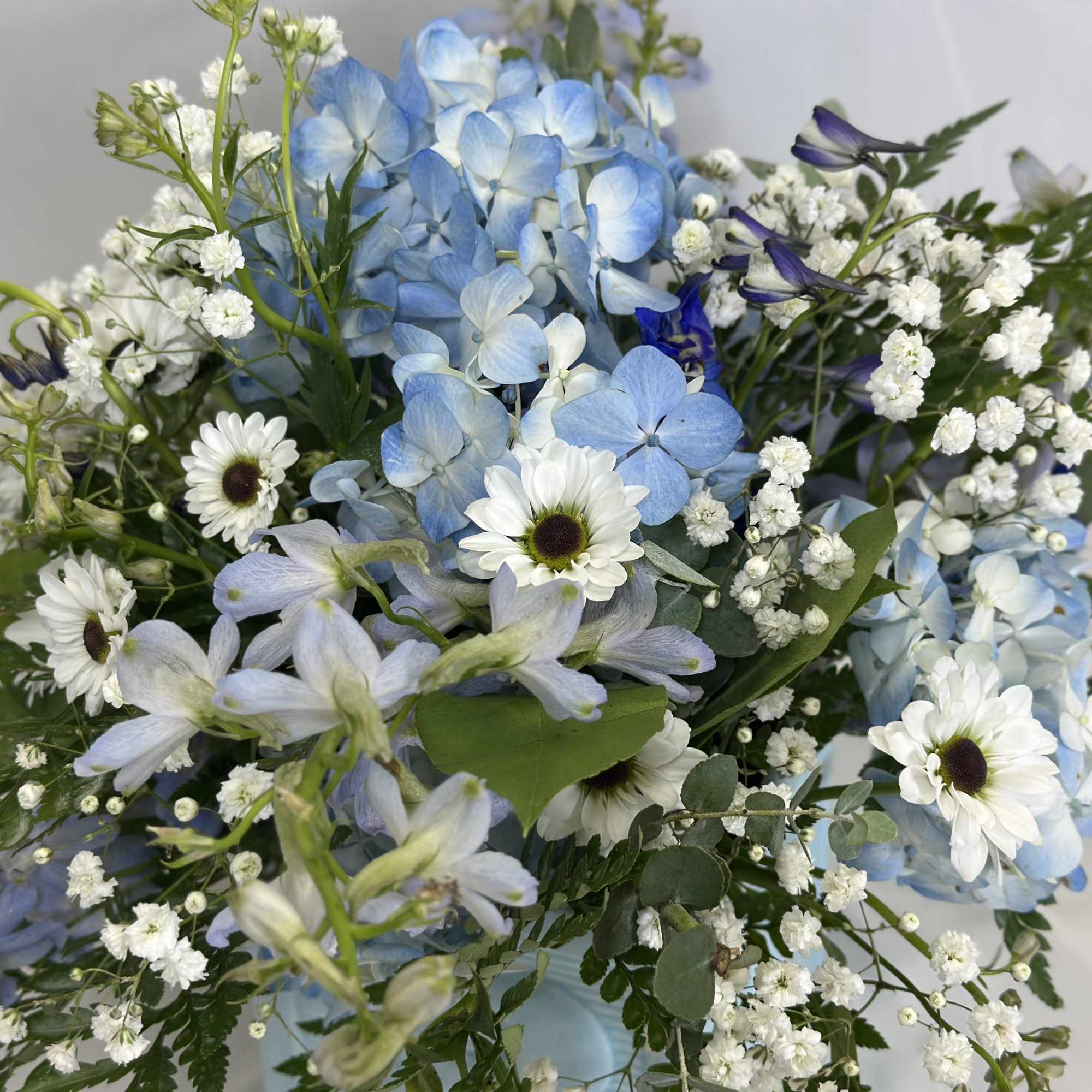 Blue hydrangeas with white daisies and small white filler flowers in a bouquet