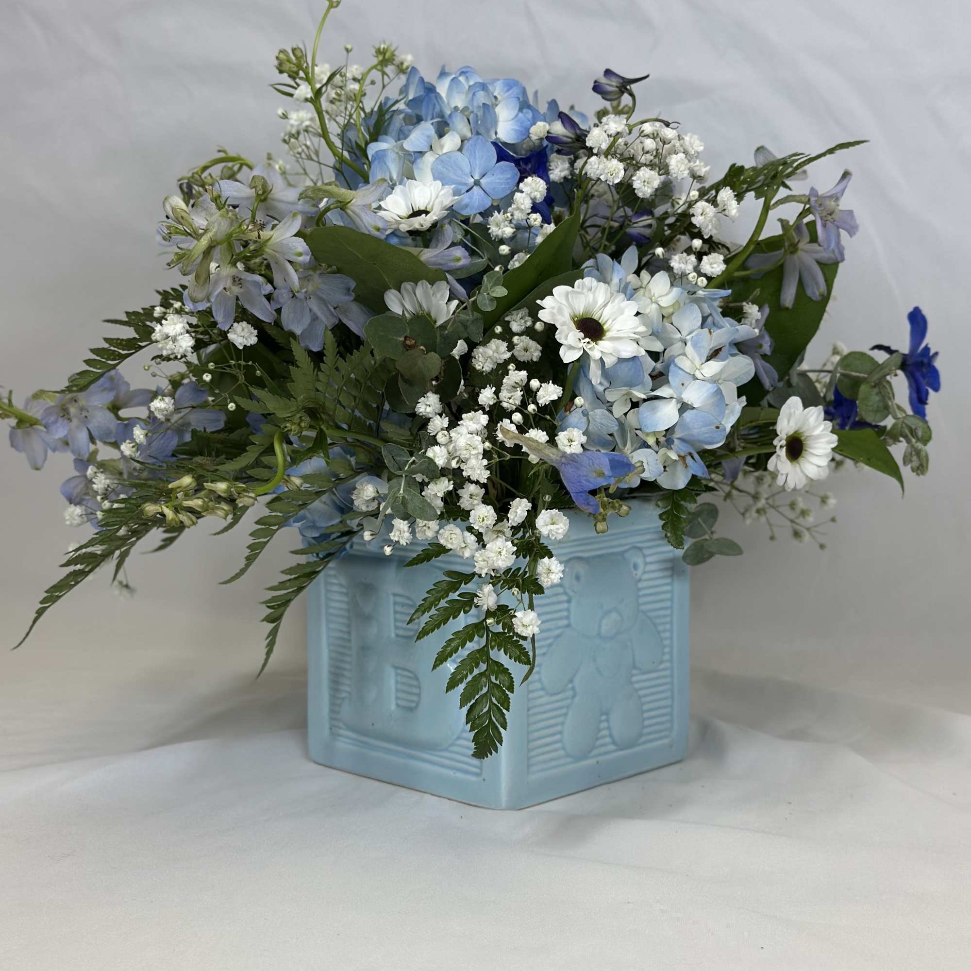 Blue and white mixed flower arrangement in a light blue vase