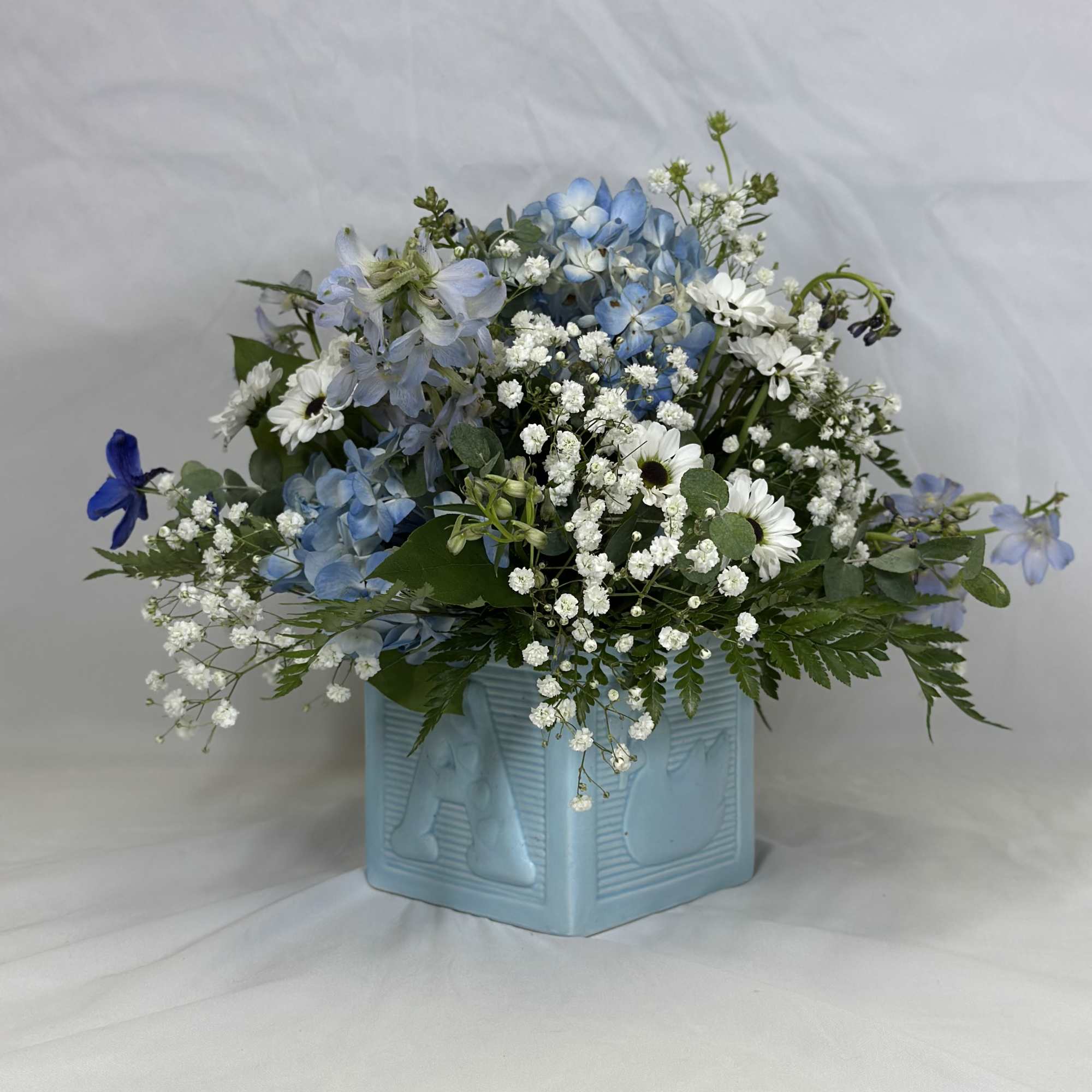 Blue and white flower arrangement in a light blue square vase