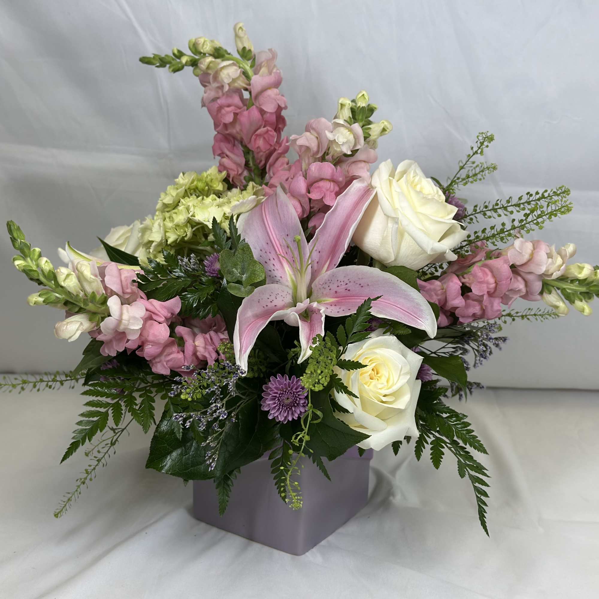 Pink lilies and white roses in a lavender vase with mixed blooms