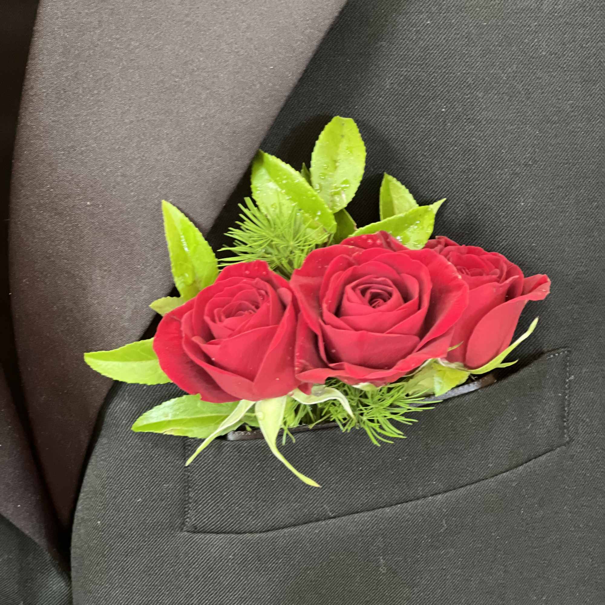 Three red roses with green accents on a black suit lapel