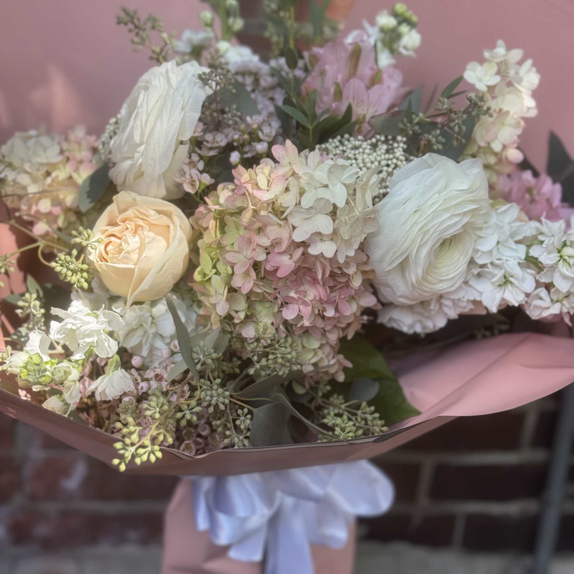 Pastel bouquet of white and blush flowers wrapped in pink paper