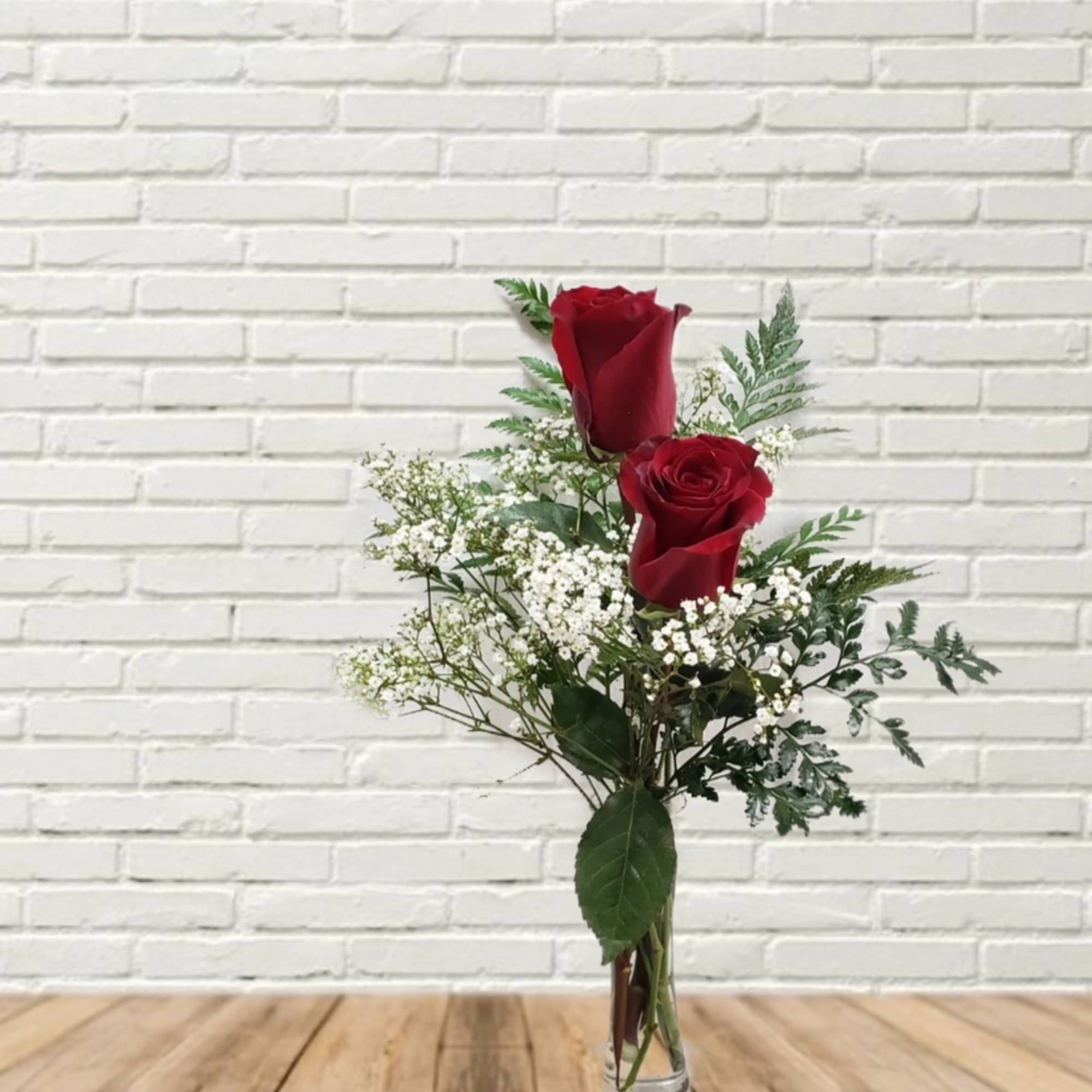 Two red roses in a small glass vase with baby's breath
