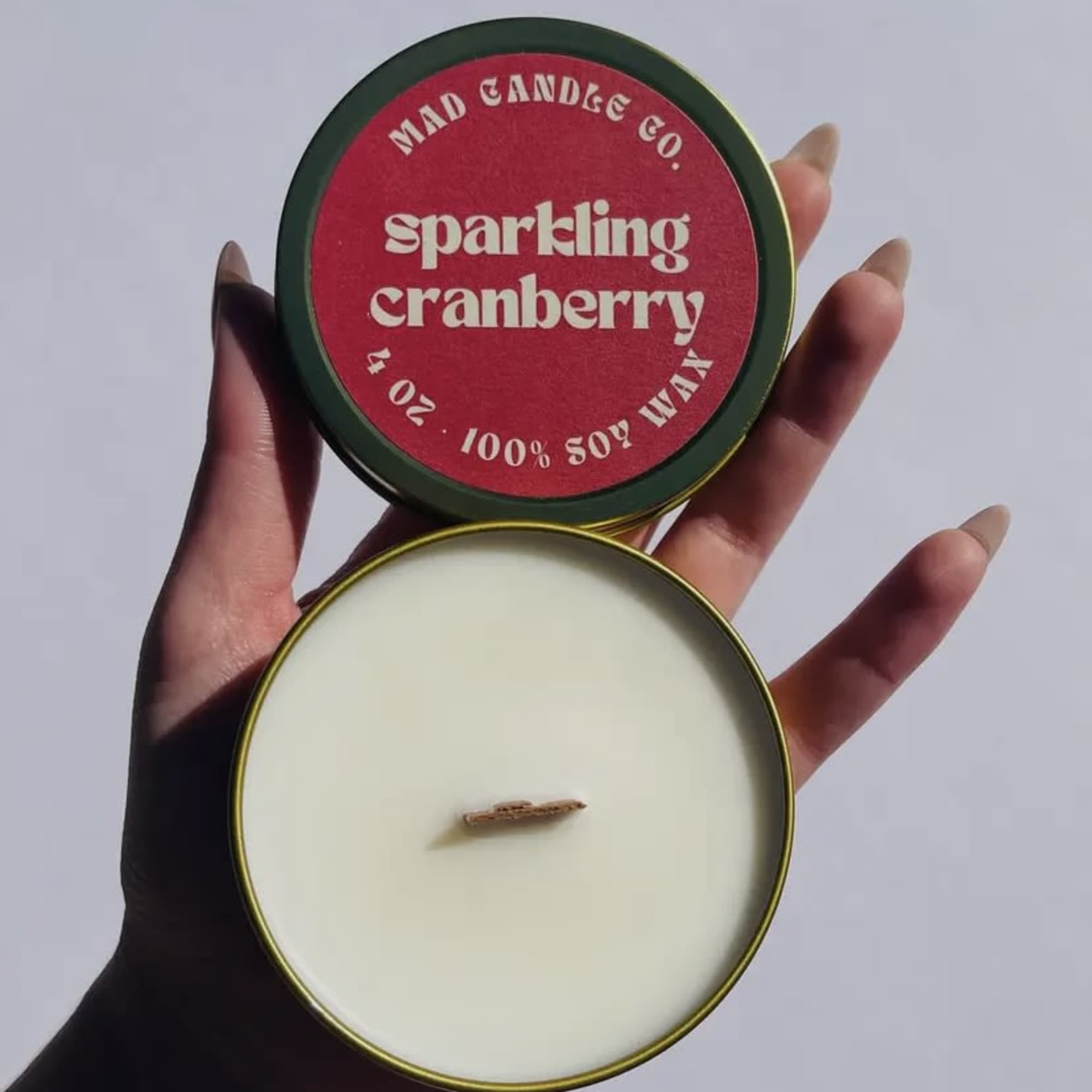 Hand holding an open tin candle labeled sparkling cranberry