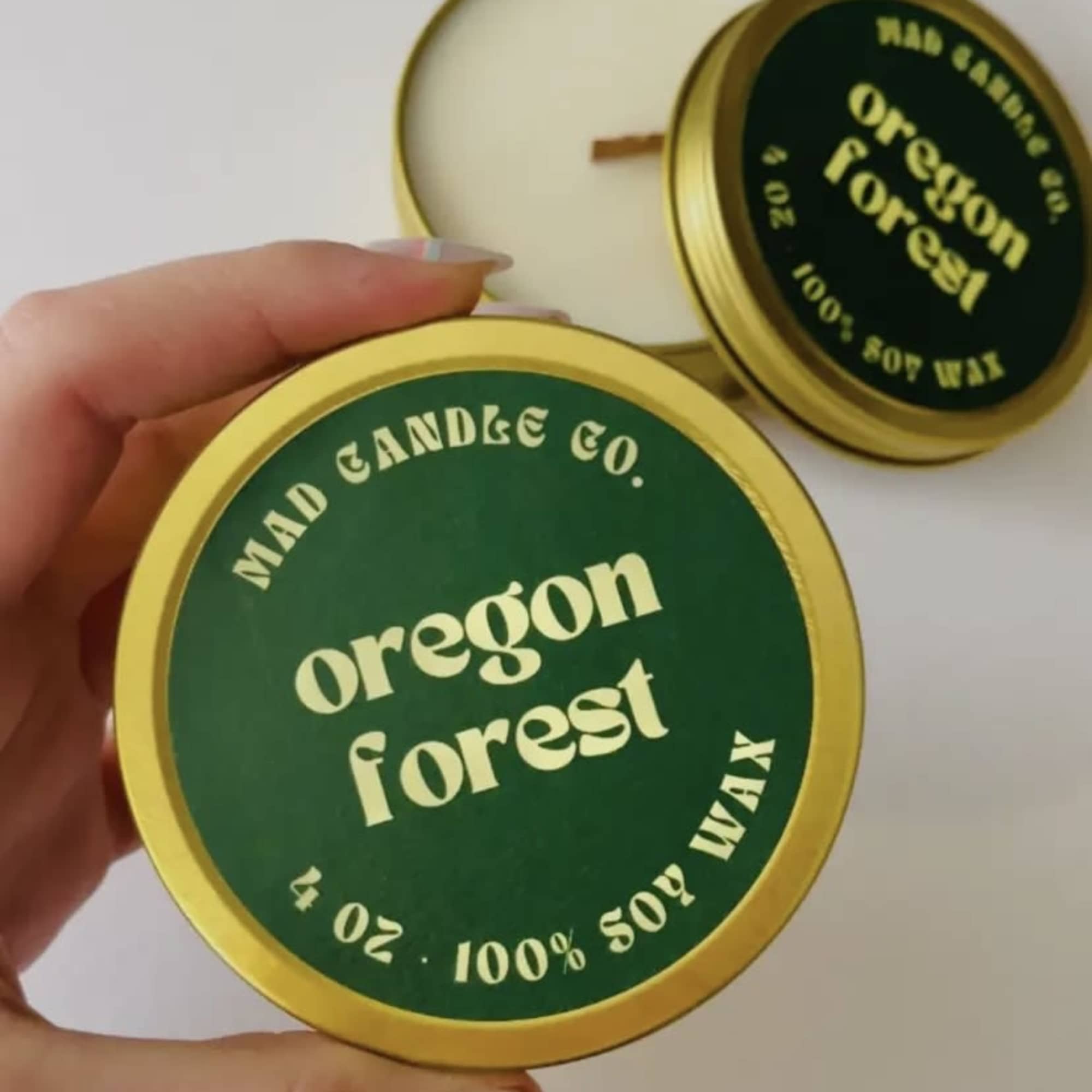 Hand holding a round green soy wax candle tin labeled Oregon Forest