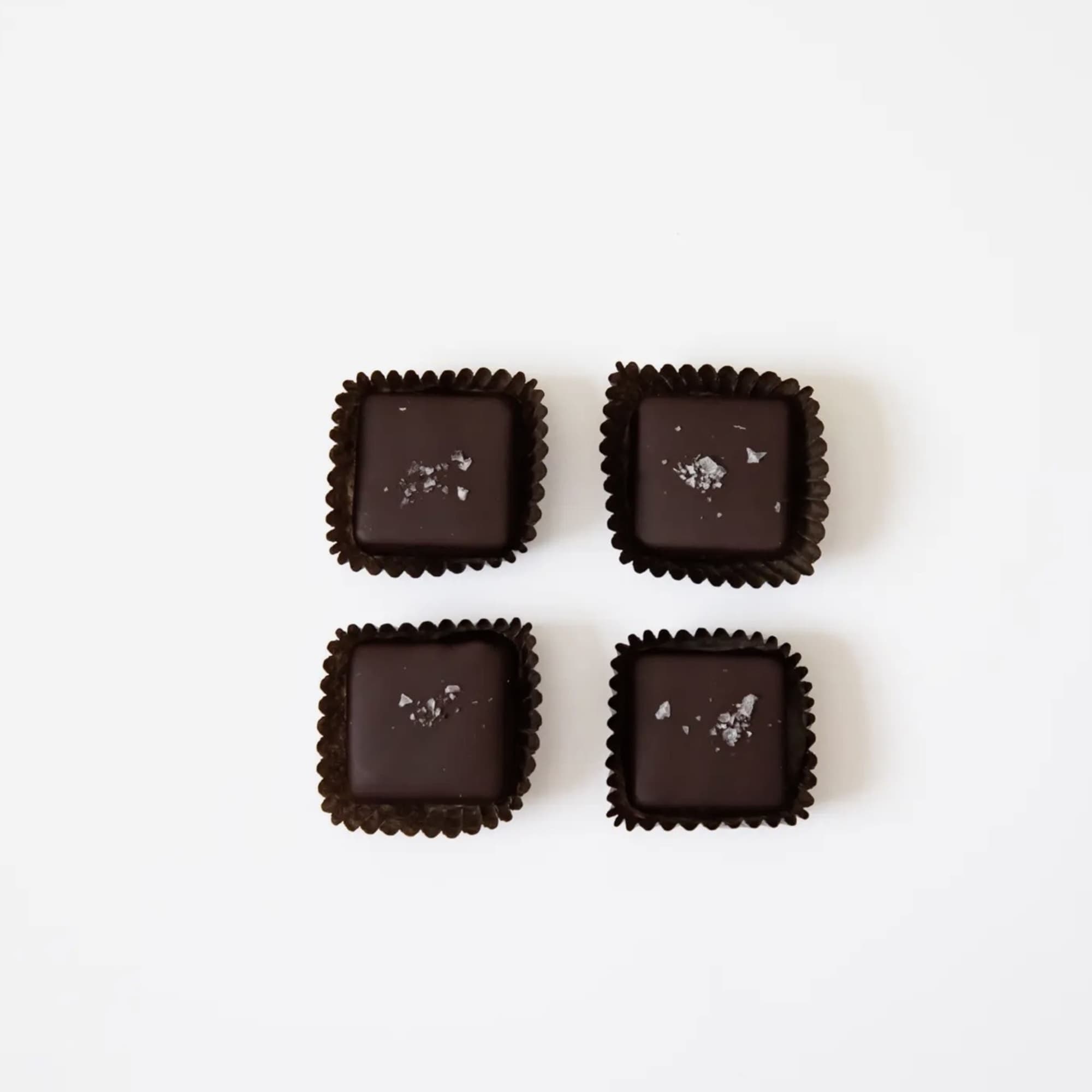 Four square dark chocolates in paper cups on a white background