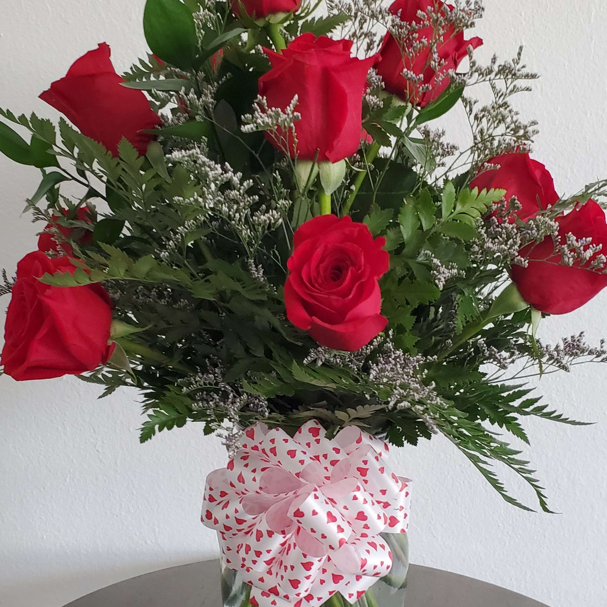 Red roses in a clear glass vase with a heart-patterned bow