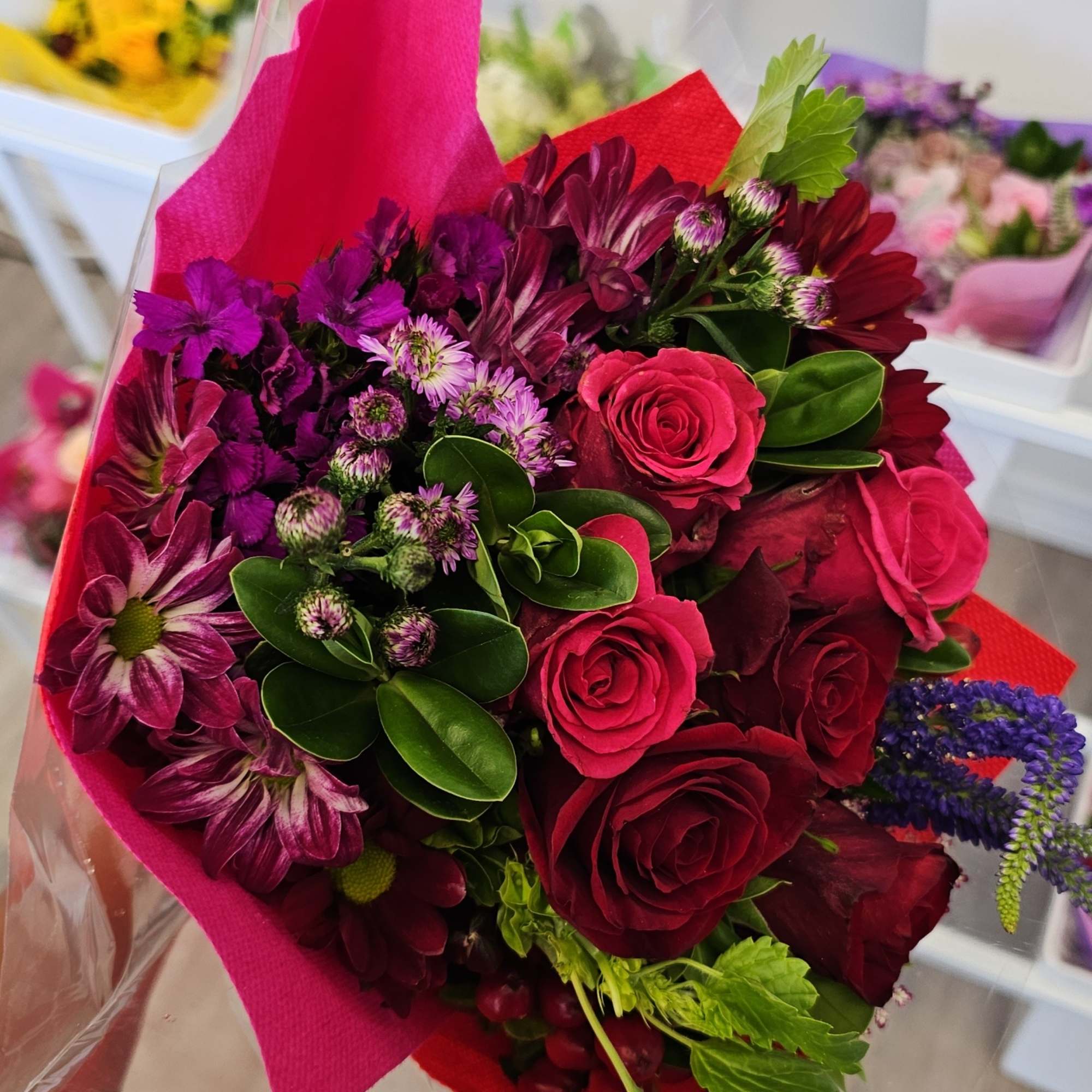 Bouquet of red roses and purple flowers wrapped in pink and red paper