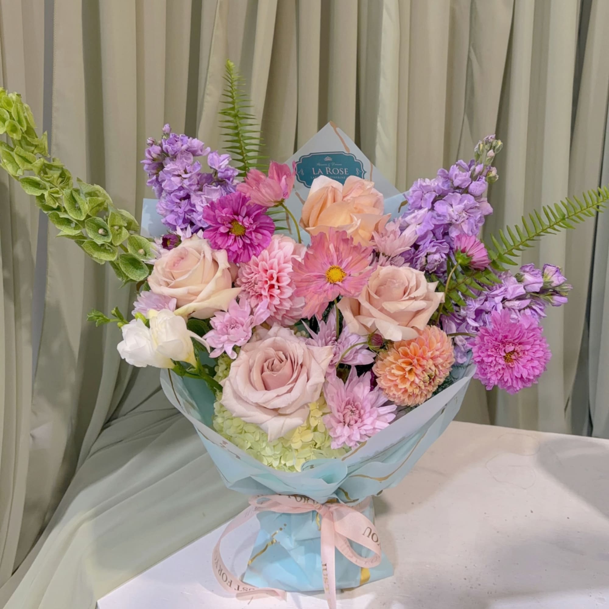 Pastel mixed bouquet with roses, dahlias, and purple blooms in blue wrapping