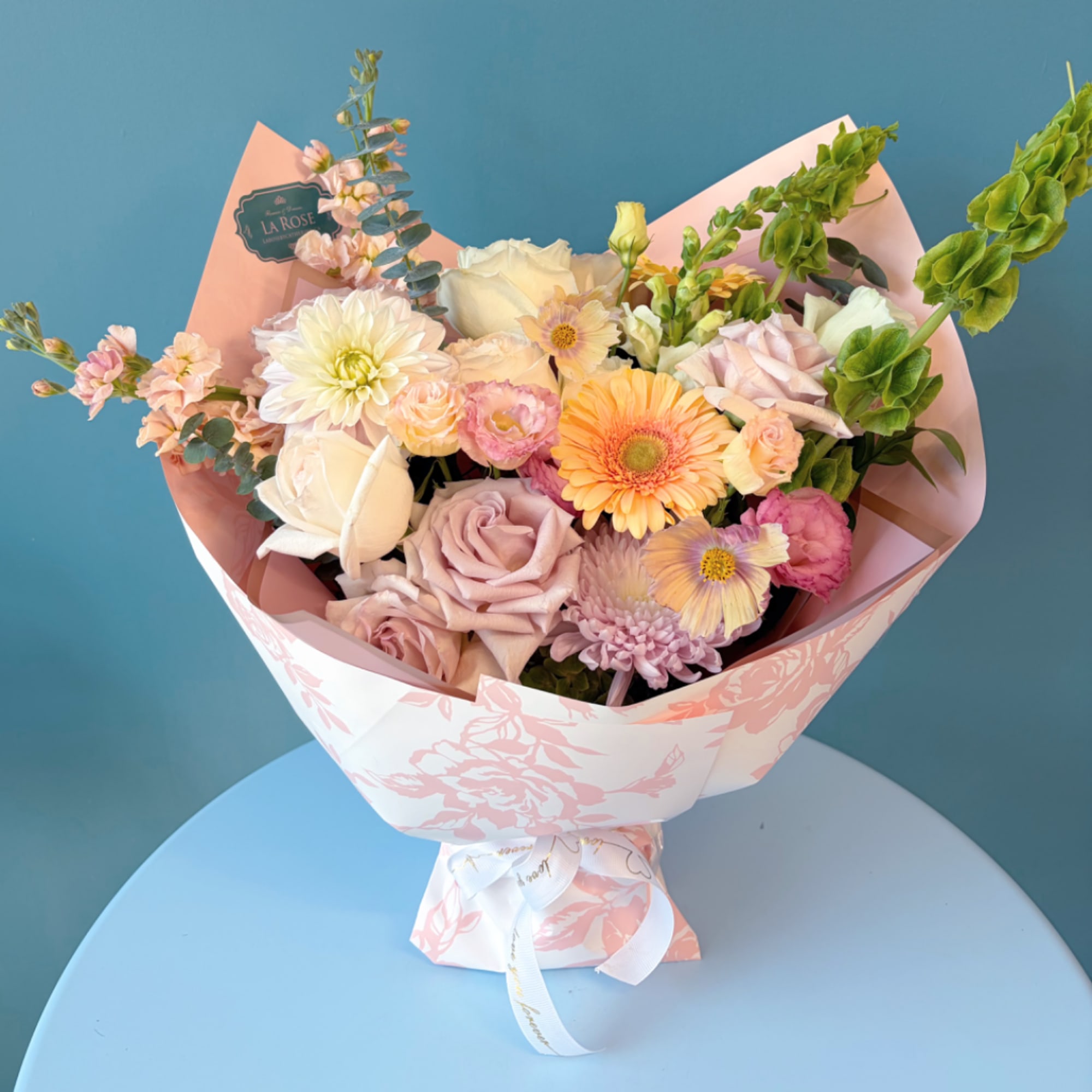 Pastel mixed flower bouquet wrapped in pink paper with a ribbon