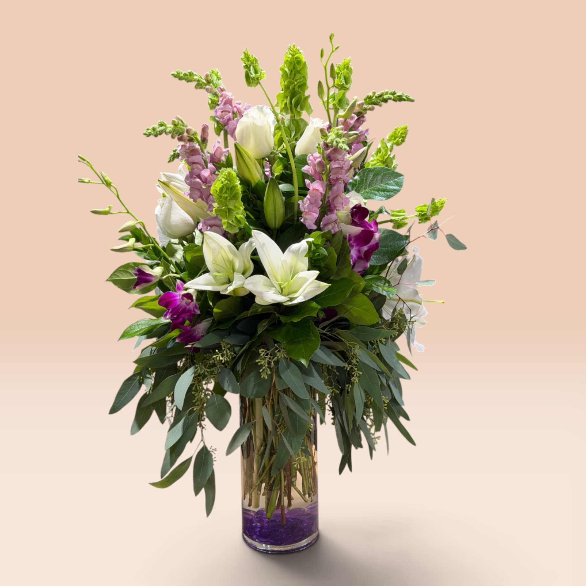 Tall bouquet of white lilies and purple flowers in a glass vase