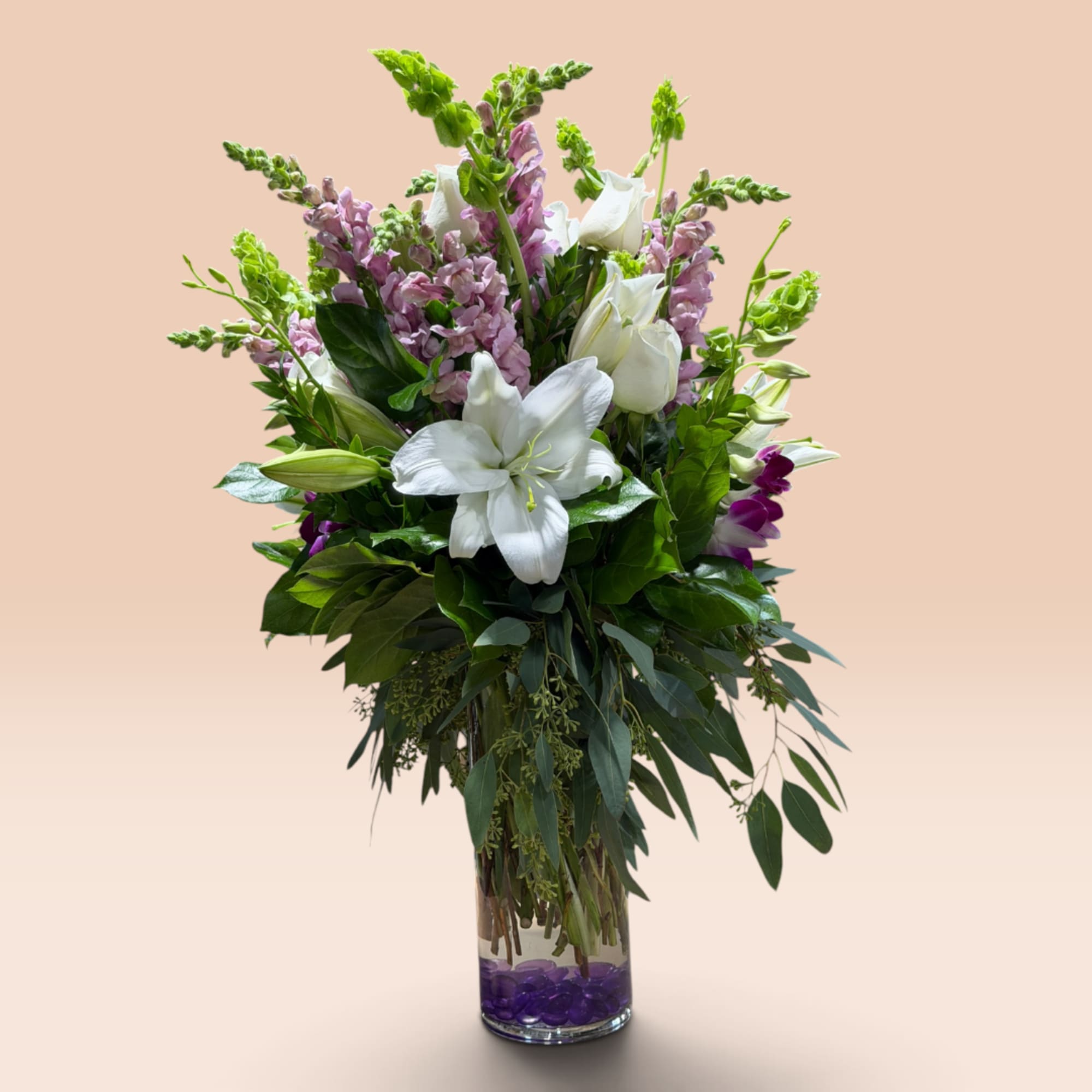 Tall bouquet of white lilies and pink snapdragons in a clear glass vase