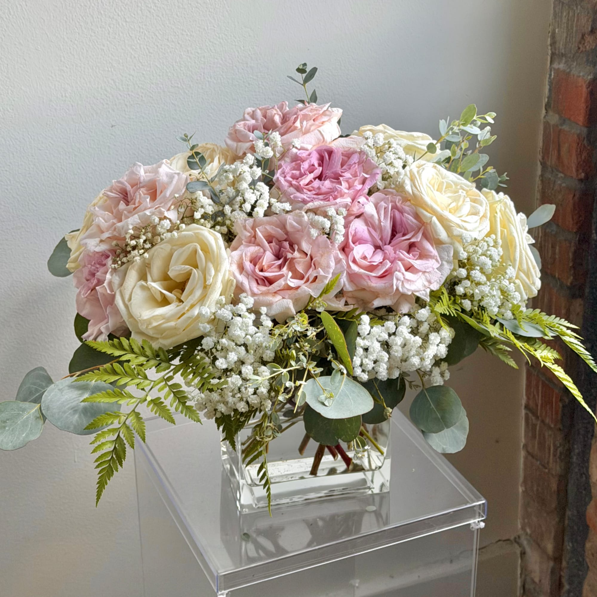 Pink and cream roses arranged in a clear square vase