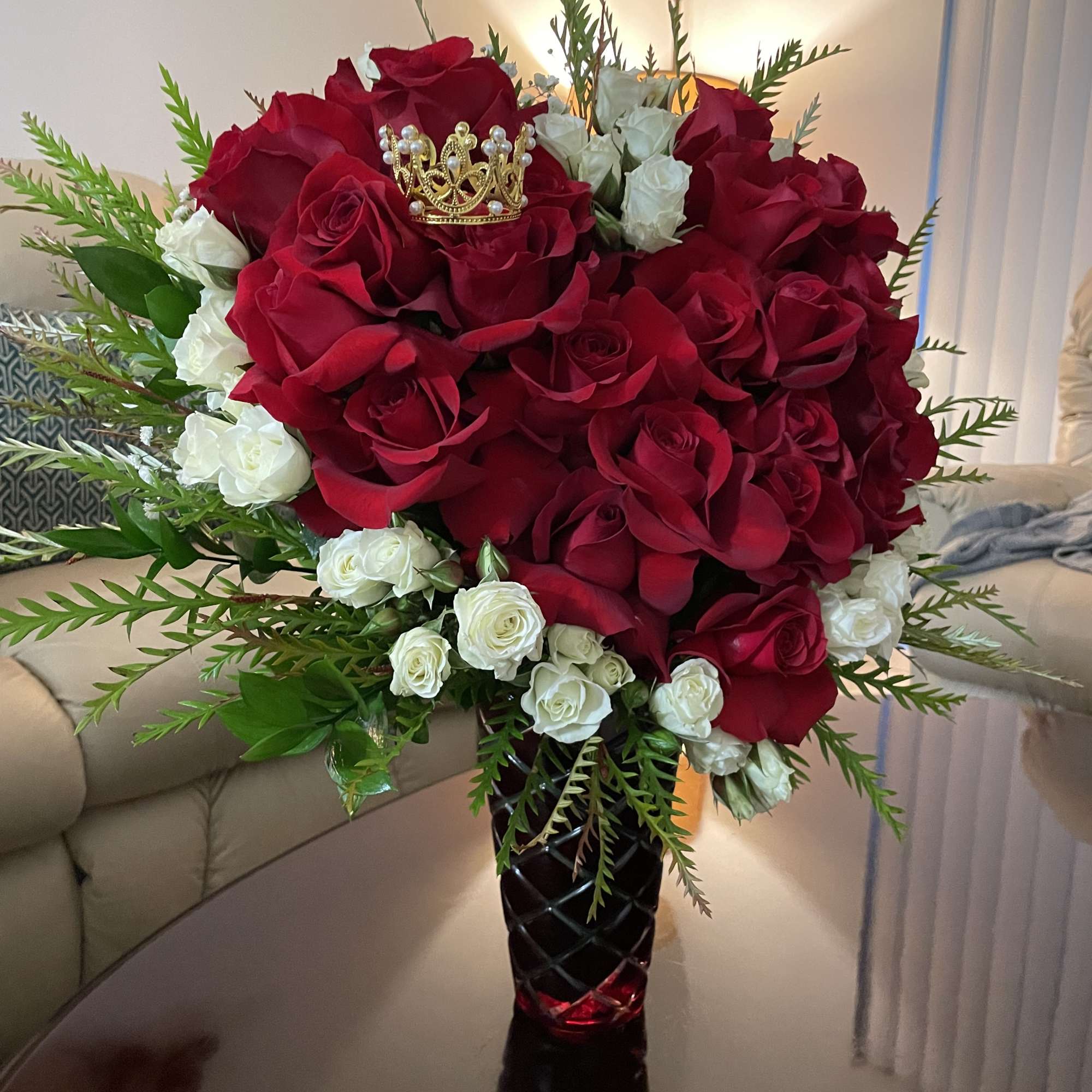 Red and white rose bouquet in a black vase with a small crown topper