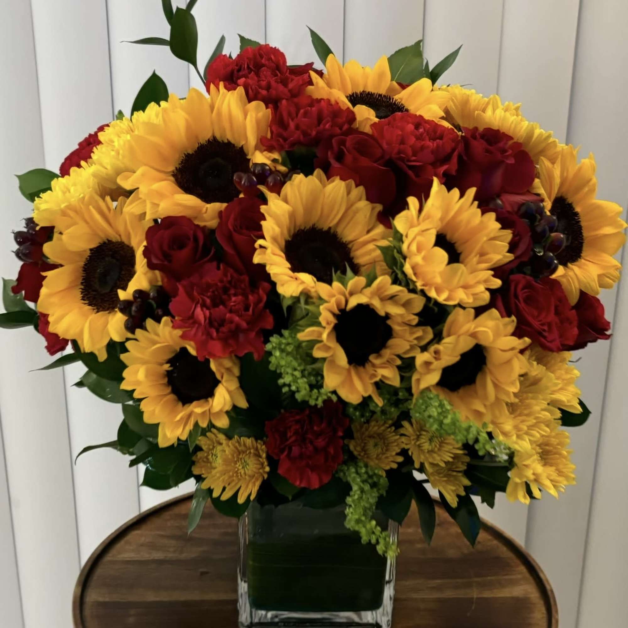 Bouquet of yellow sunflowers and red roses in a clear square vase