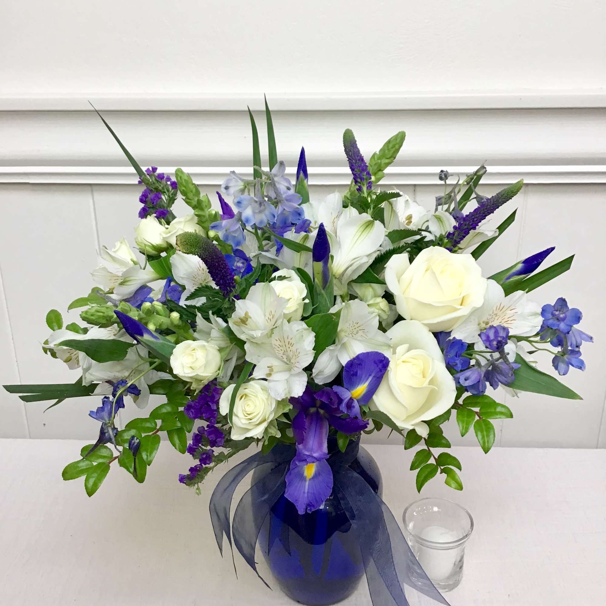 White and blue floral arrangement in a blue vase with ribbon