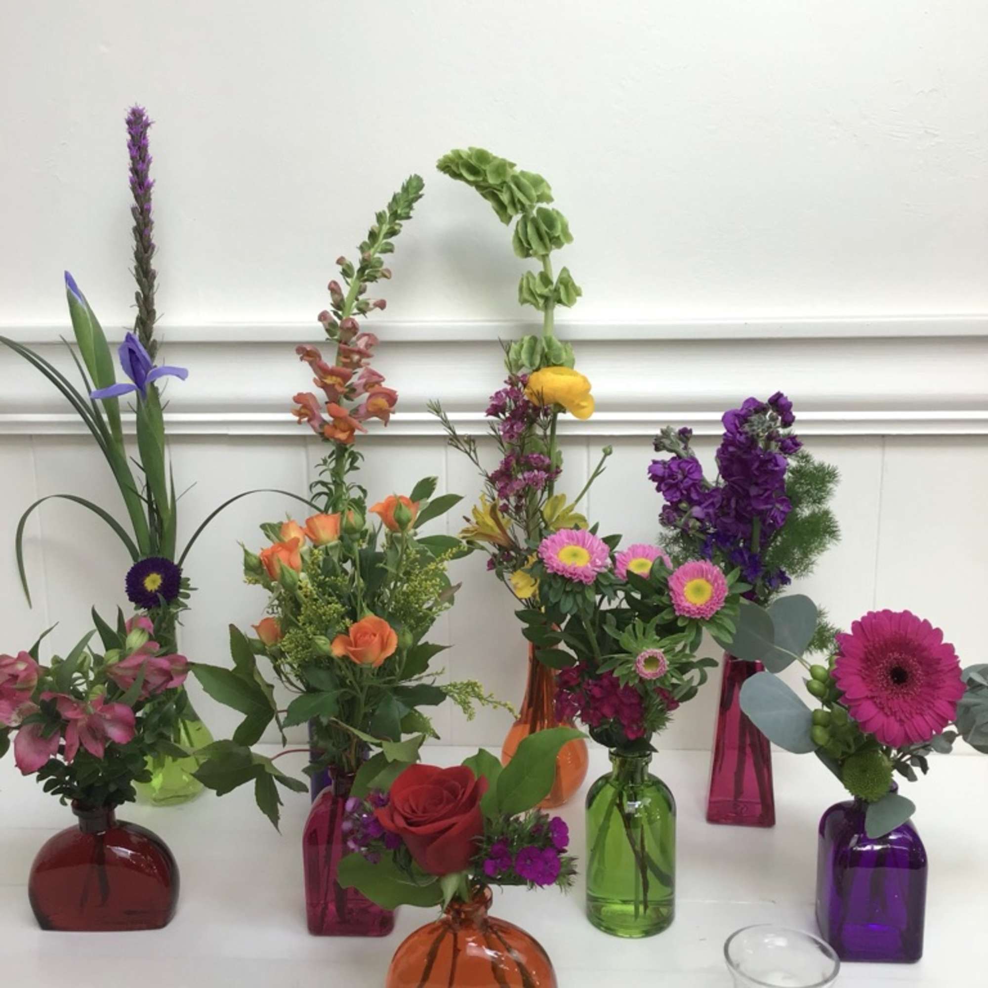 Assorted colorful flower arrangements in small glass vases on a white table