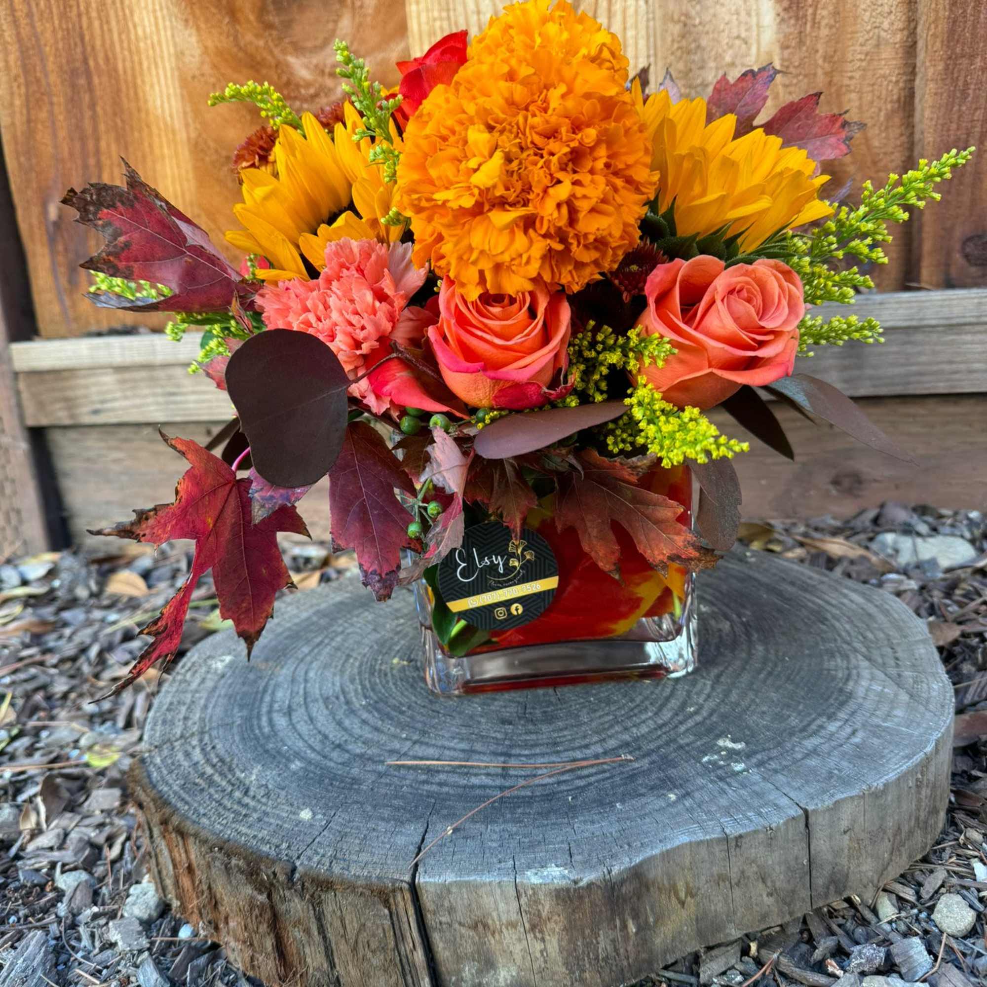 Autumn bouquet with sunflowers, orange roses, and marigolds in a glass vase