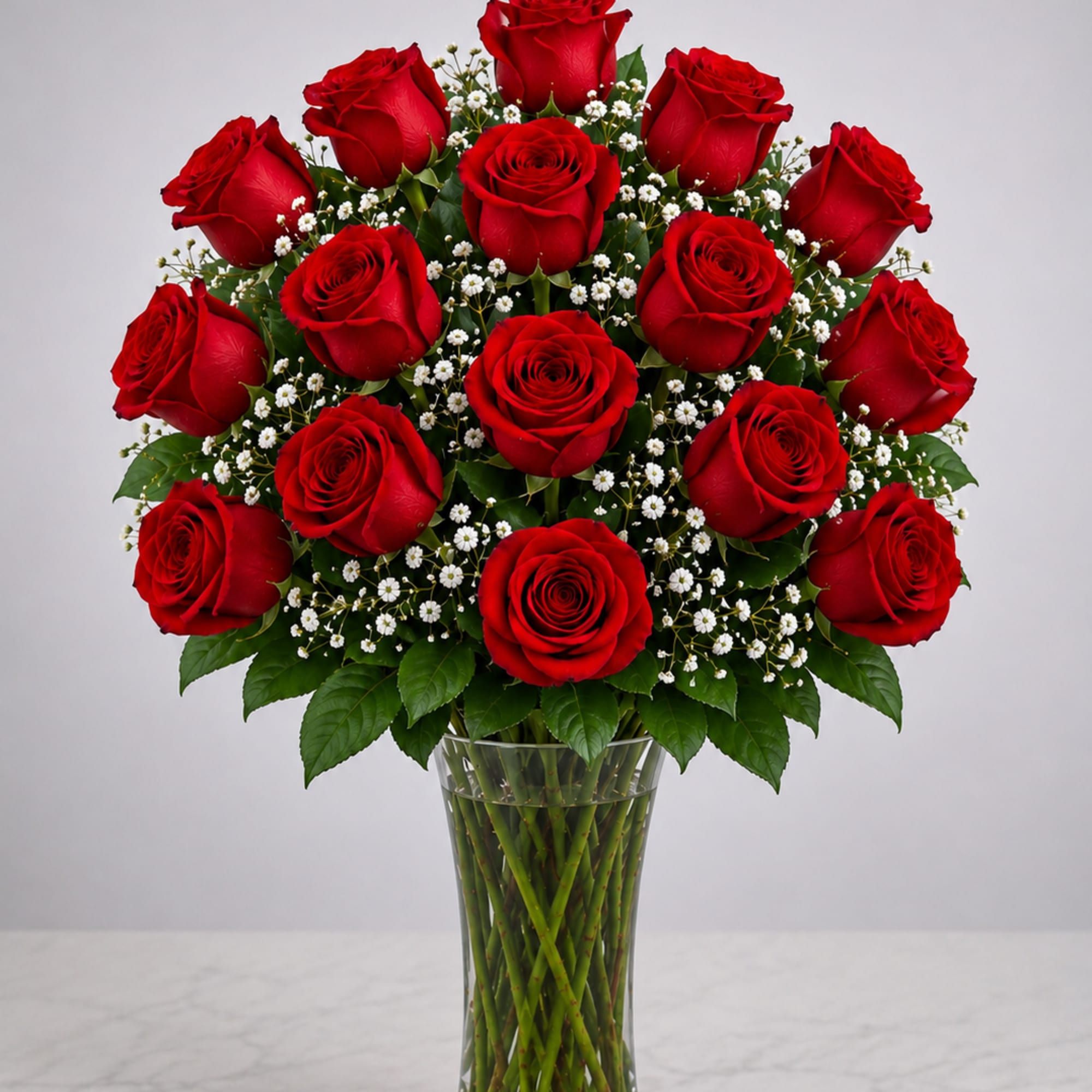 Red roses arranged in a clear glass vase with small white filler flowers