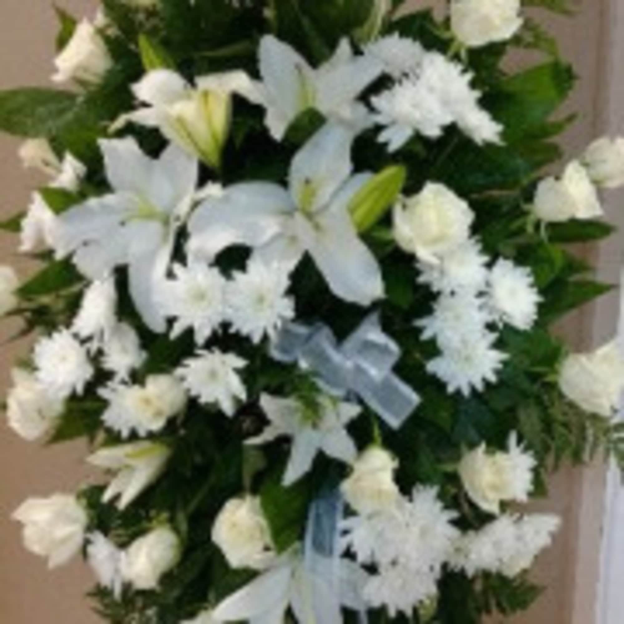White lilies and chrysanthemums in a standing floral spray with blue ribbon