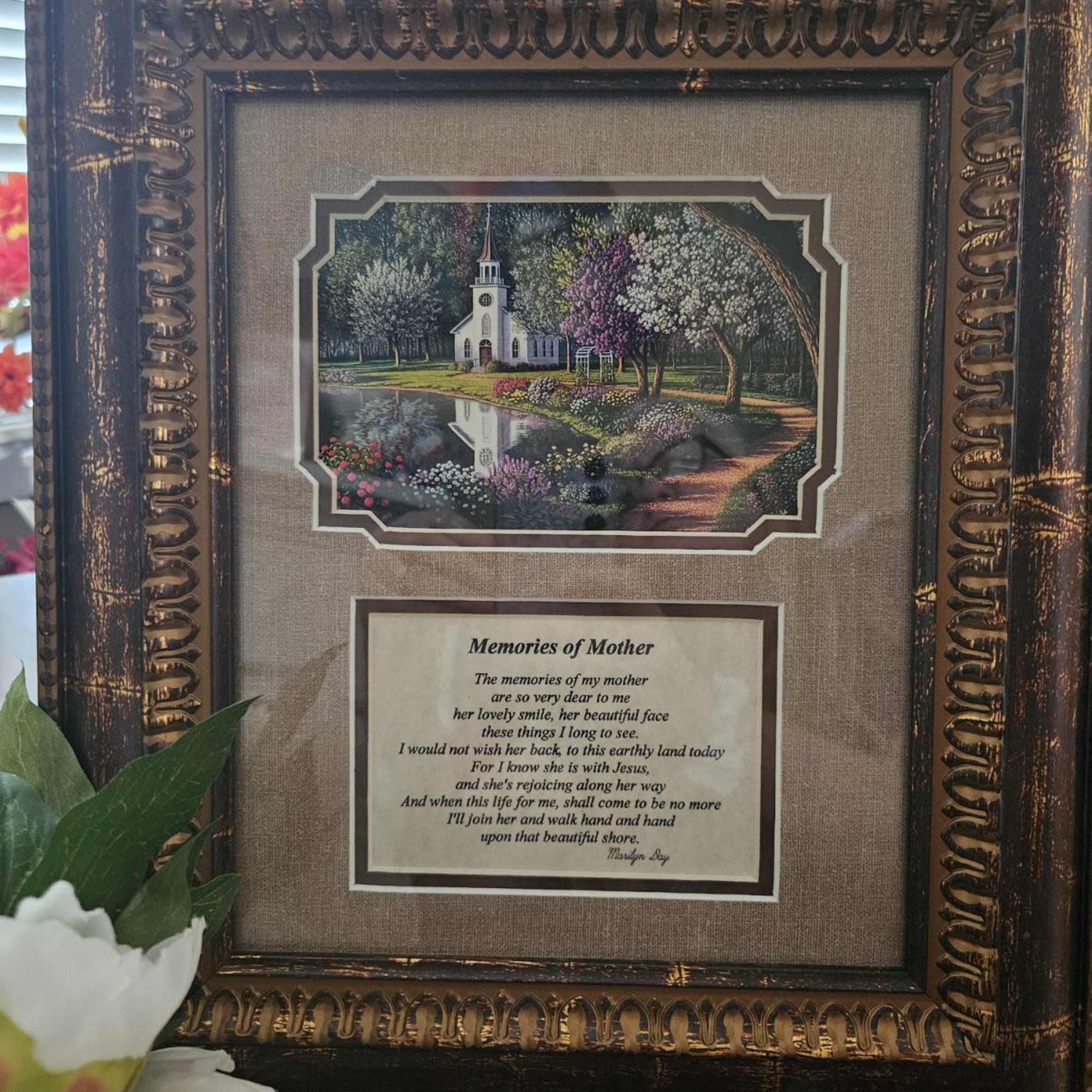 Framed memorial plaque with a church scene and poem, with white flowers at the bottom