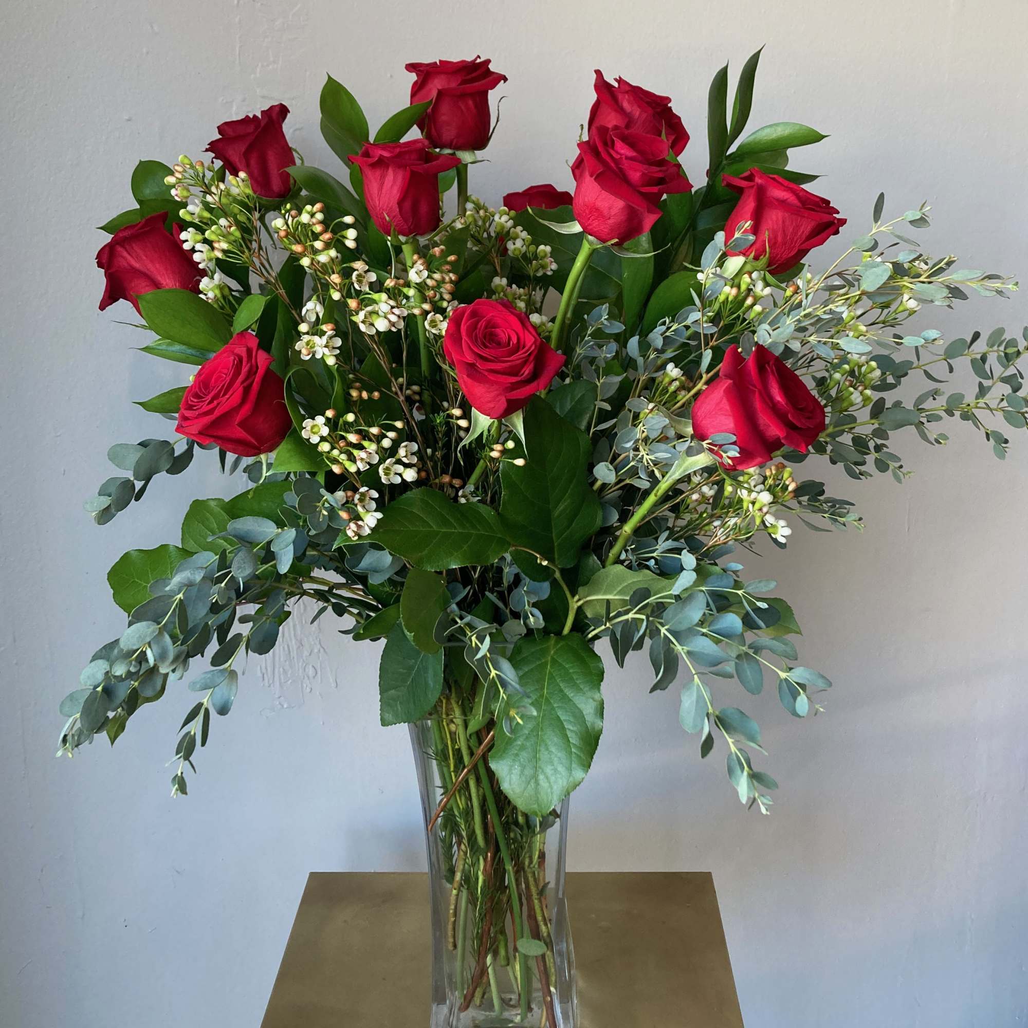 Red roses arranged in a clear glass vase with mixed greenery