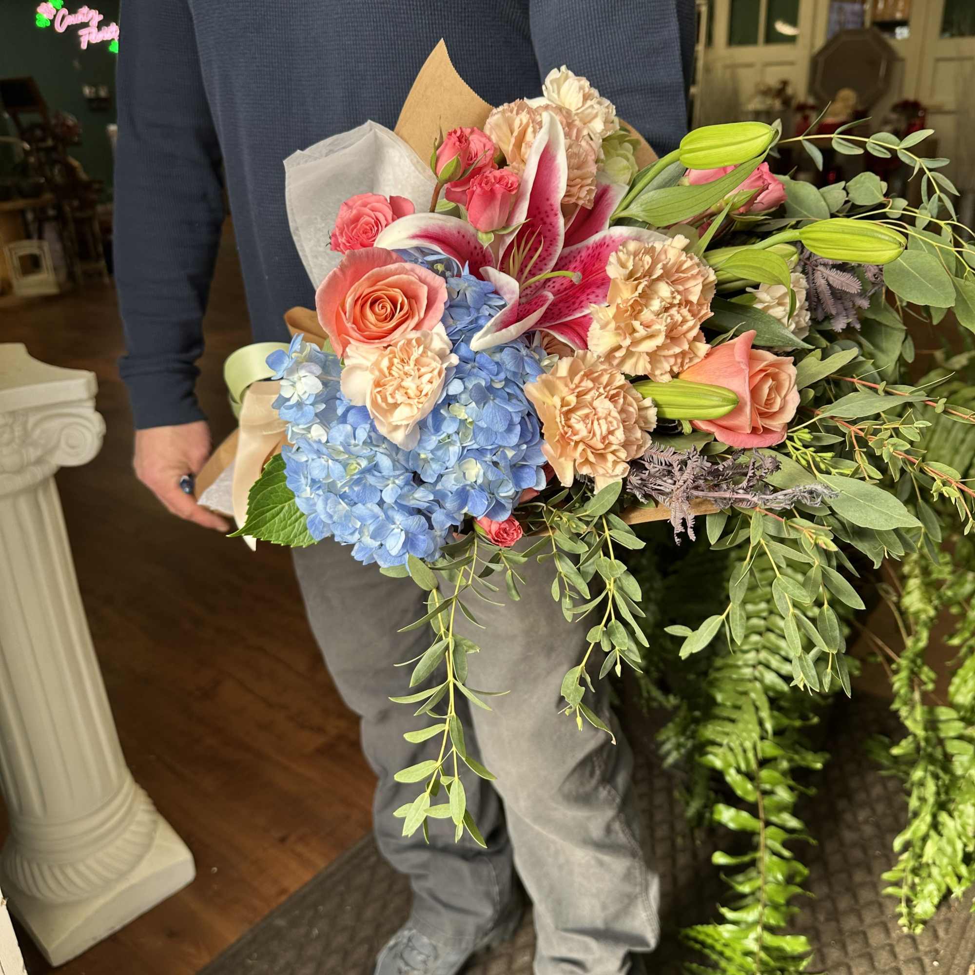 Handheld bouquet with pink roses, blue hydrangea, lilies, and greenery