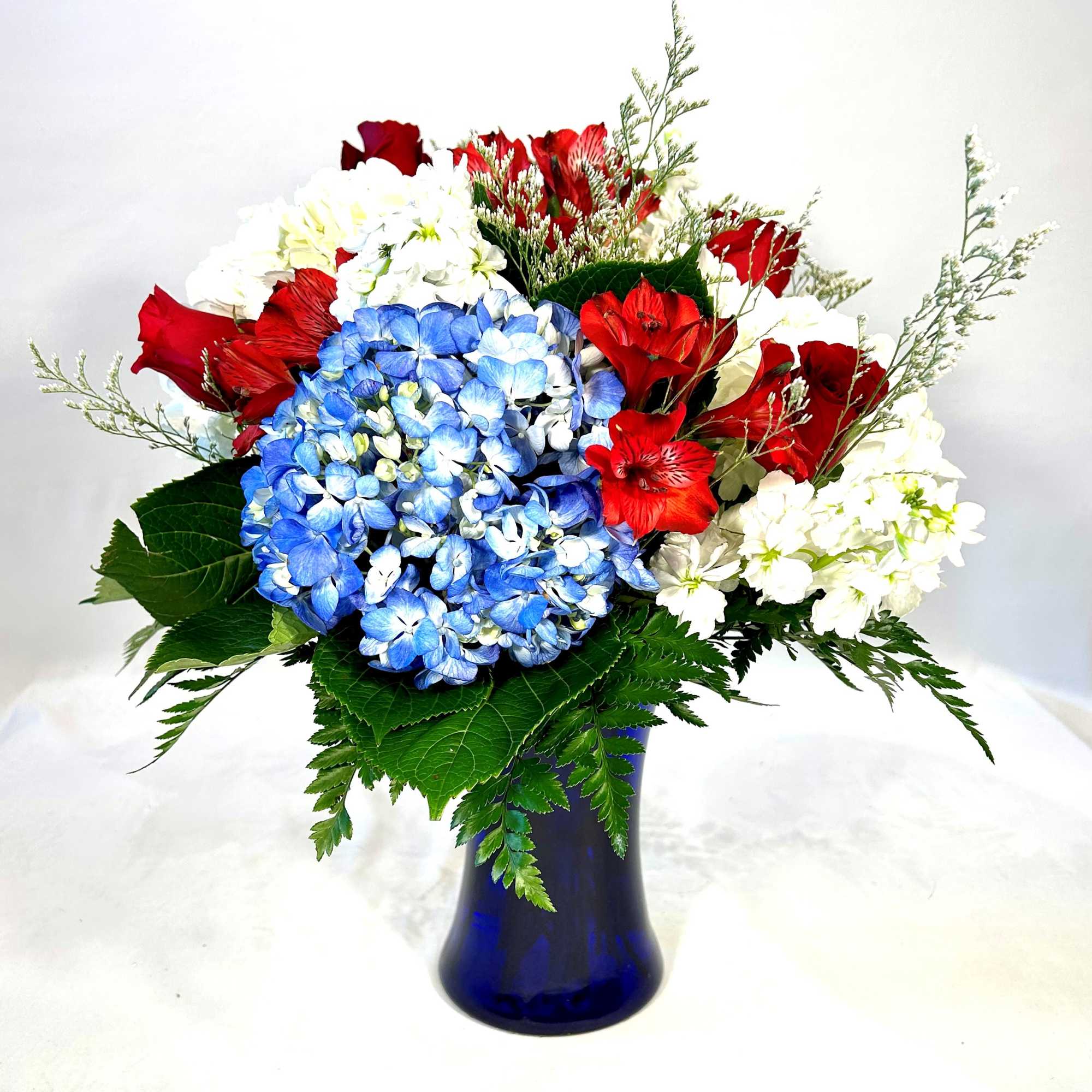 Bouquet of red roses, blue hydrangeas, and white flowers in a blue vase