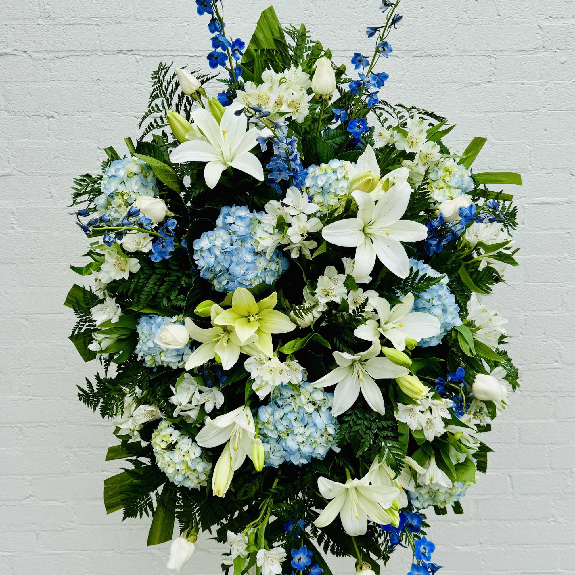 Large standing floral spray with white lilies, blue flowers, and hydrangeas