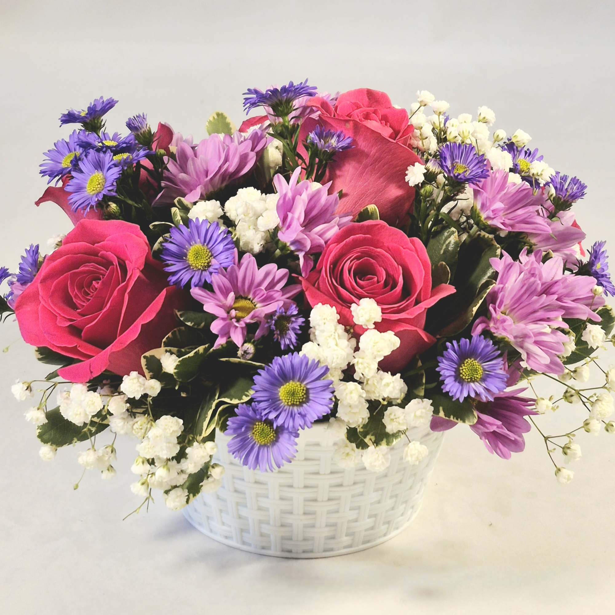 Pink roses and purple daisies in a white basket