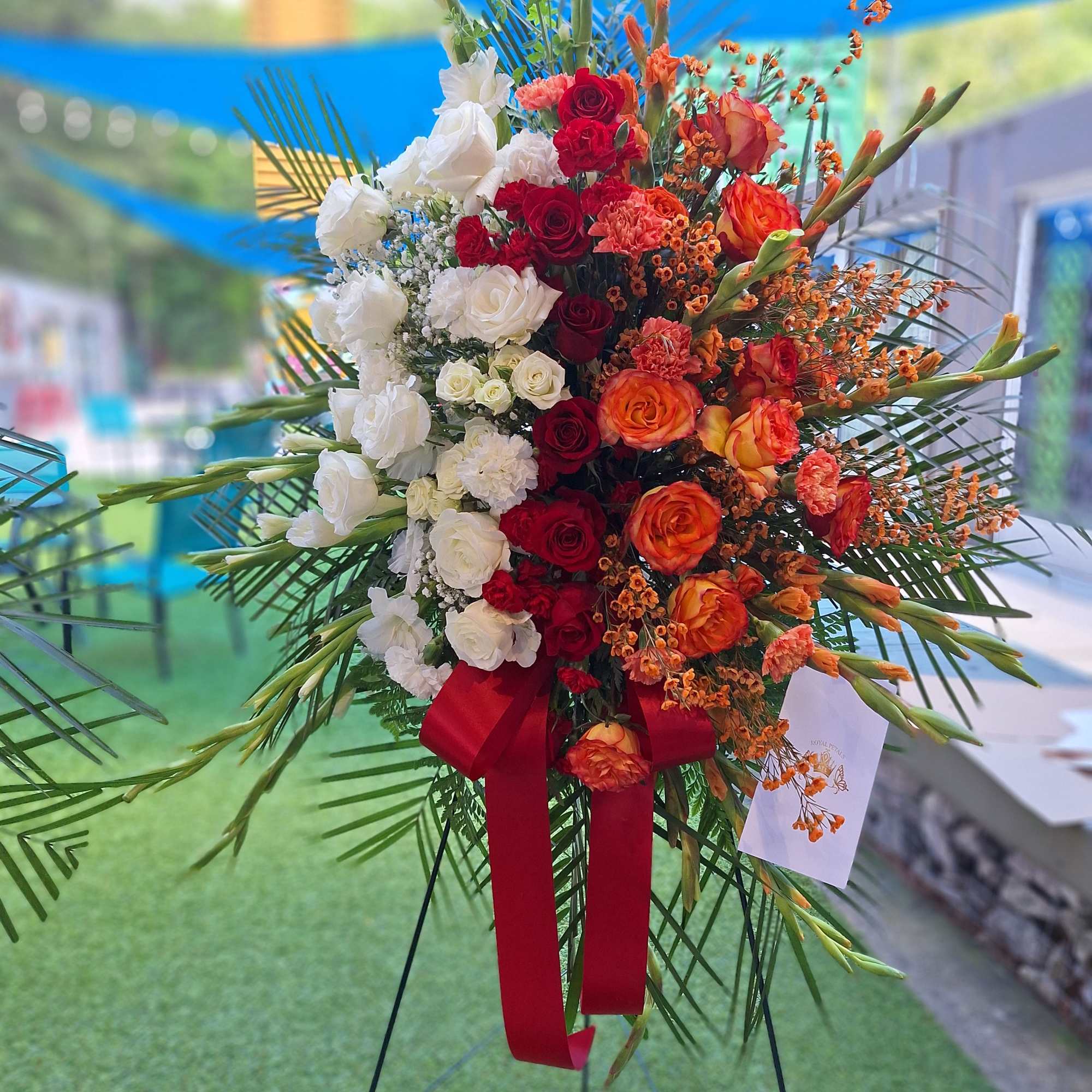 Tall standing floral spray with red, white, and orange roses on an easel