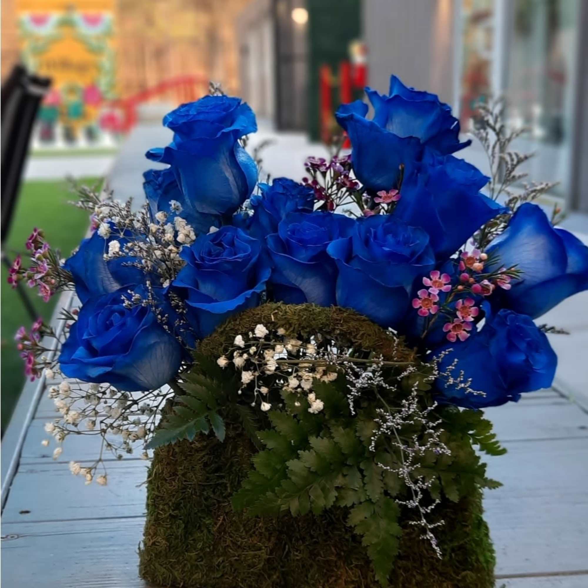 Blue roses arranged in a moss-covered box with small filler flowers