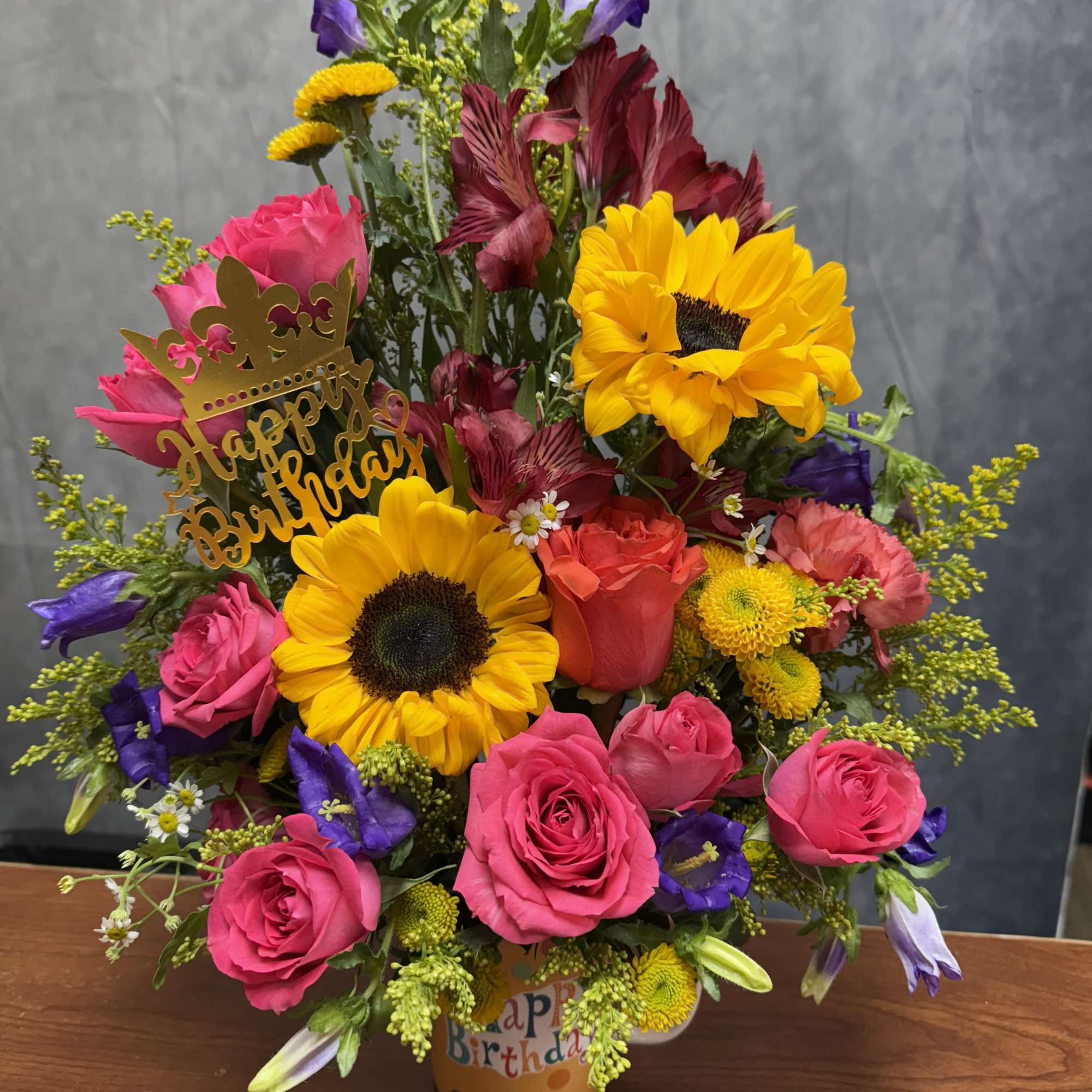Birthday bouquet with sunflowers, pink roses, and purple blooms in a decorated pot