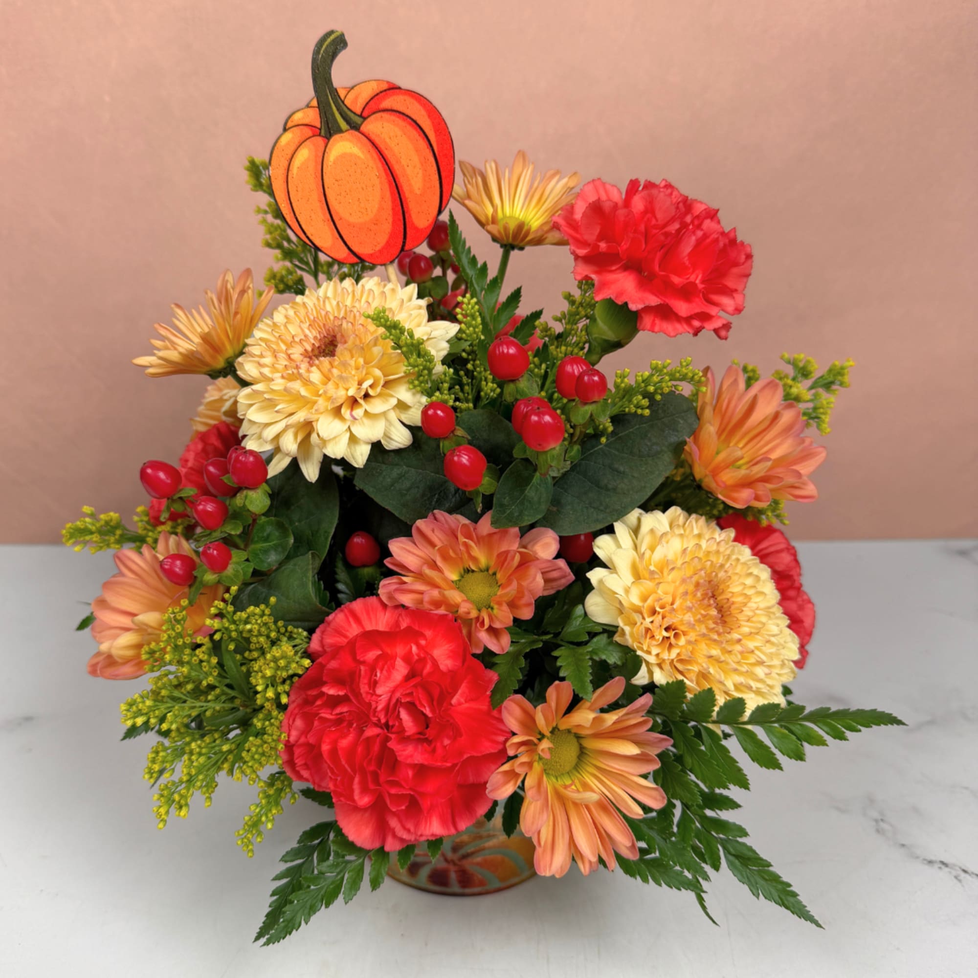 Autumn bouquet with orange and red flowers and a pumpkin pick in a vase
