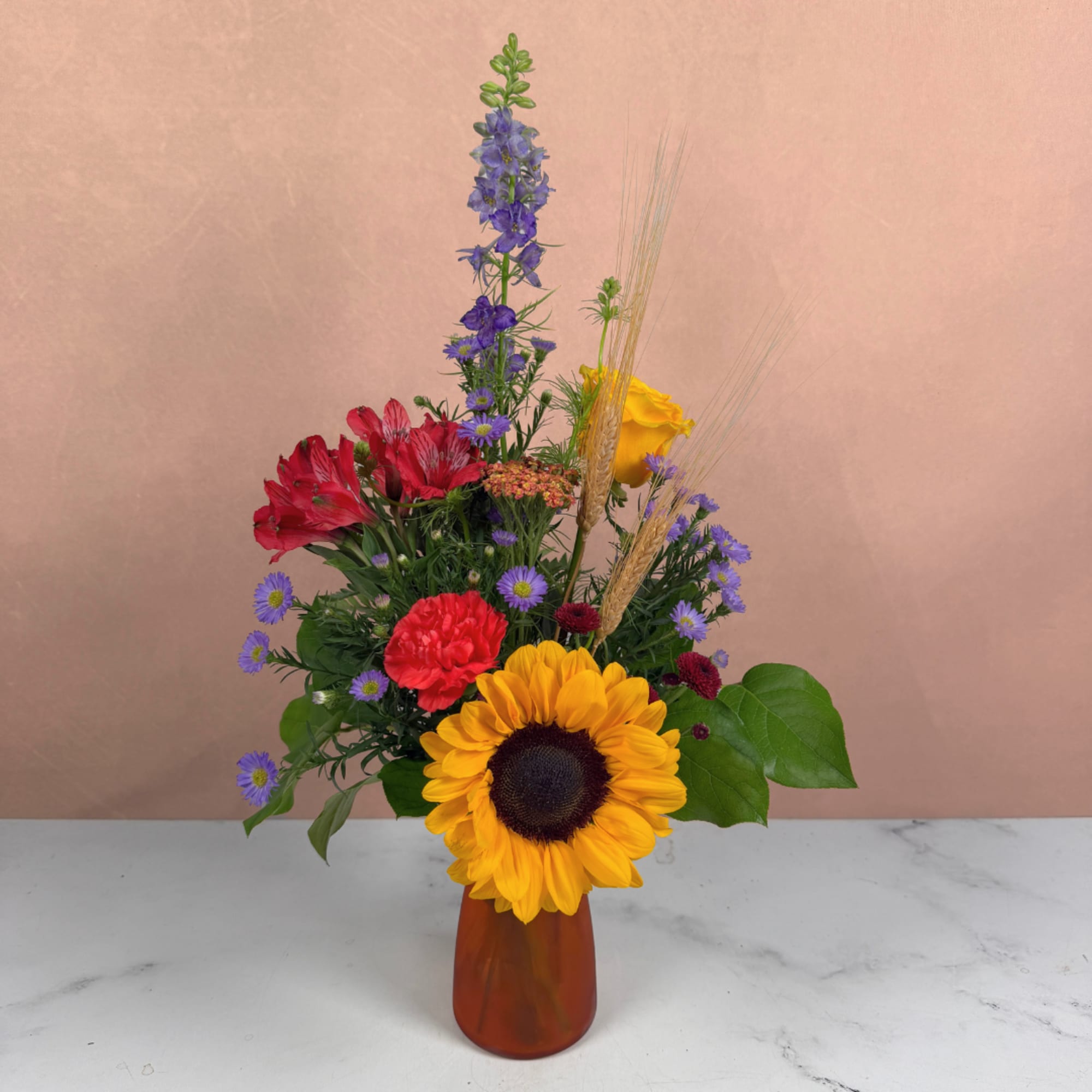 Mixed bouquet with a sunflower, red blooms, and purple flowers in an amber vase, photo 2 of 3