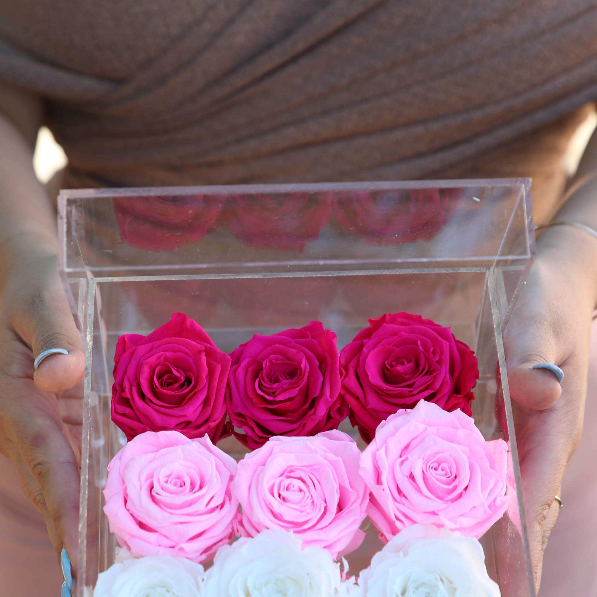Clear box of pink, red, and white roses held in hands