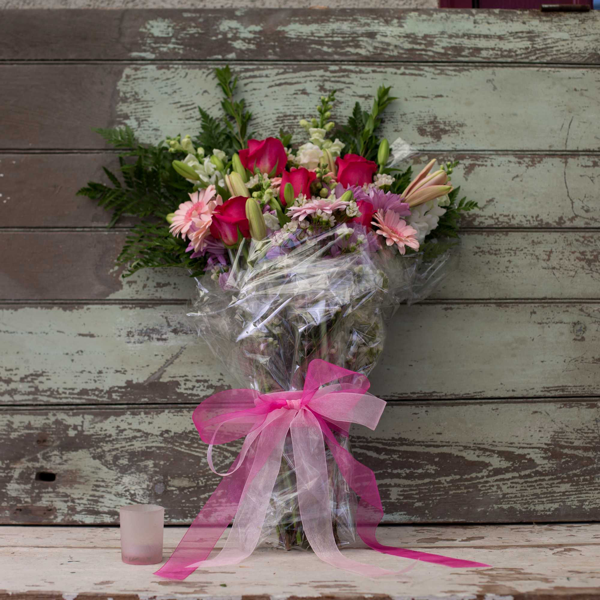 Bouquet of pink and white flowers wrapped in clear plastic with a pink ribbon
