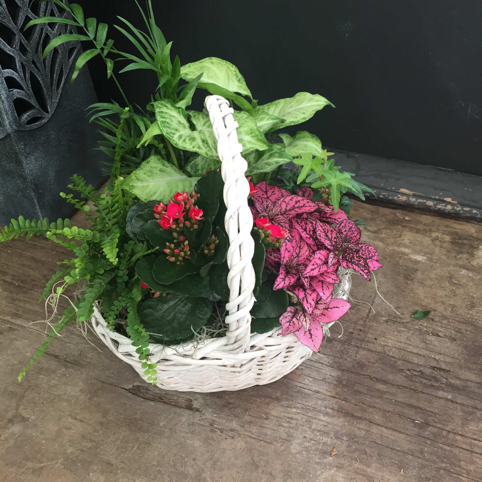 White wicker basket with assorted potted plants and pink flowering foliage