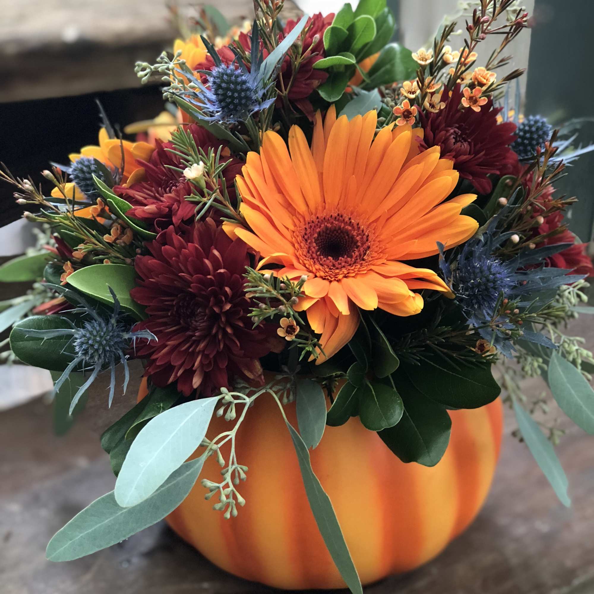 Orange and burgundy floral arrangement in a pumpkin container
