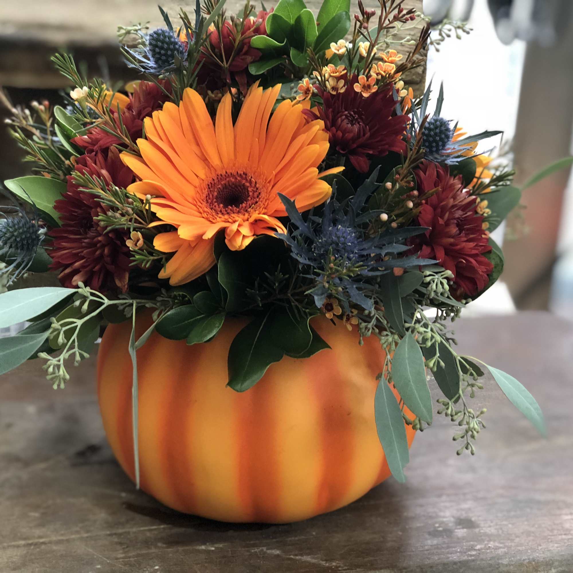 Orange and burgundy floral arrangement in a pumpkin-shaped container