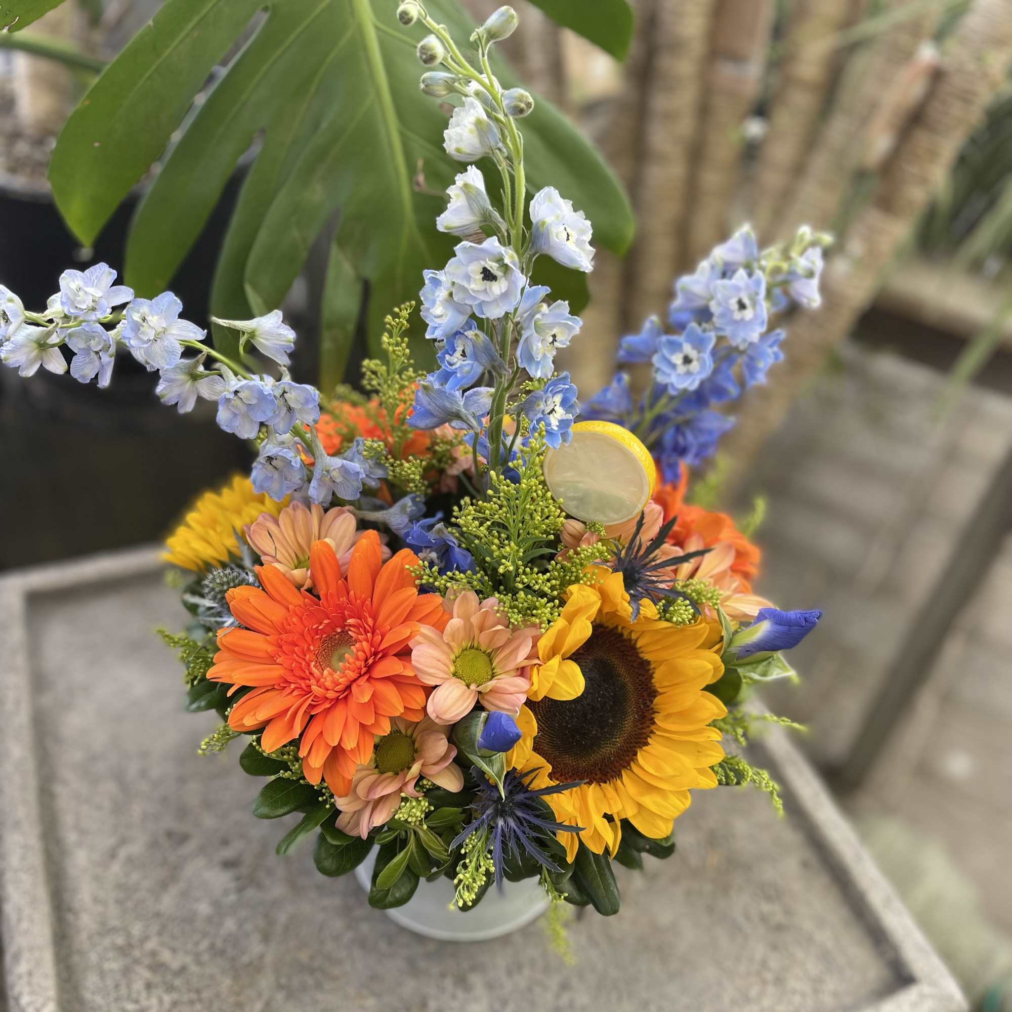 Colorful mixed bouquet with sunflowers, gerbera daisies, and blue delphinium in a vase