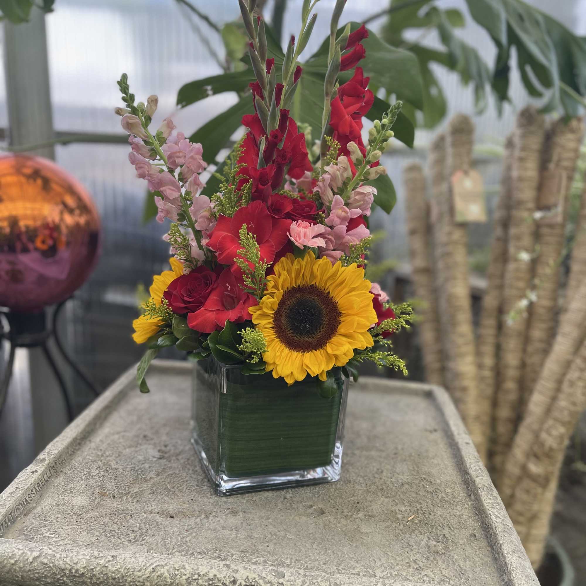 Mixed bouquet in a square glass vase with a sunflower and red blooms