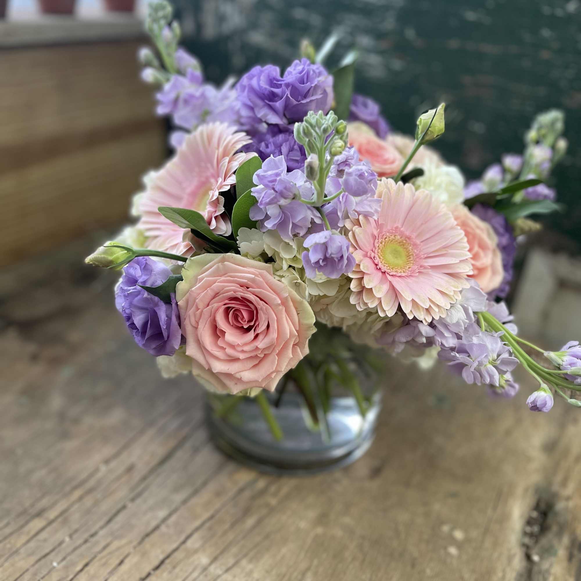 Pastel bouquet of pink roses, lavender blooms, and pale gerbera daisies in a glass vase