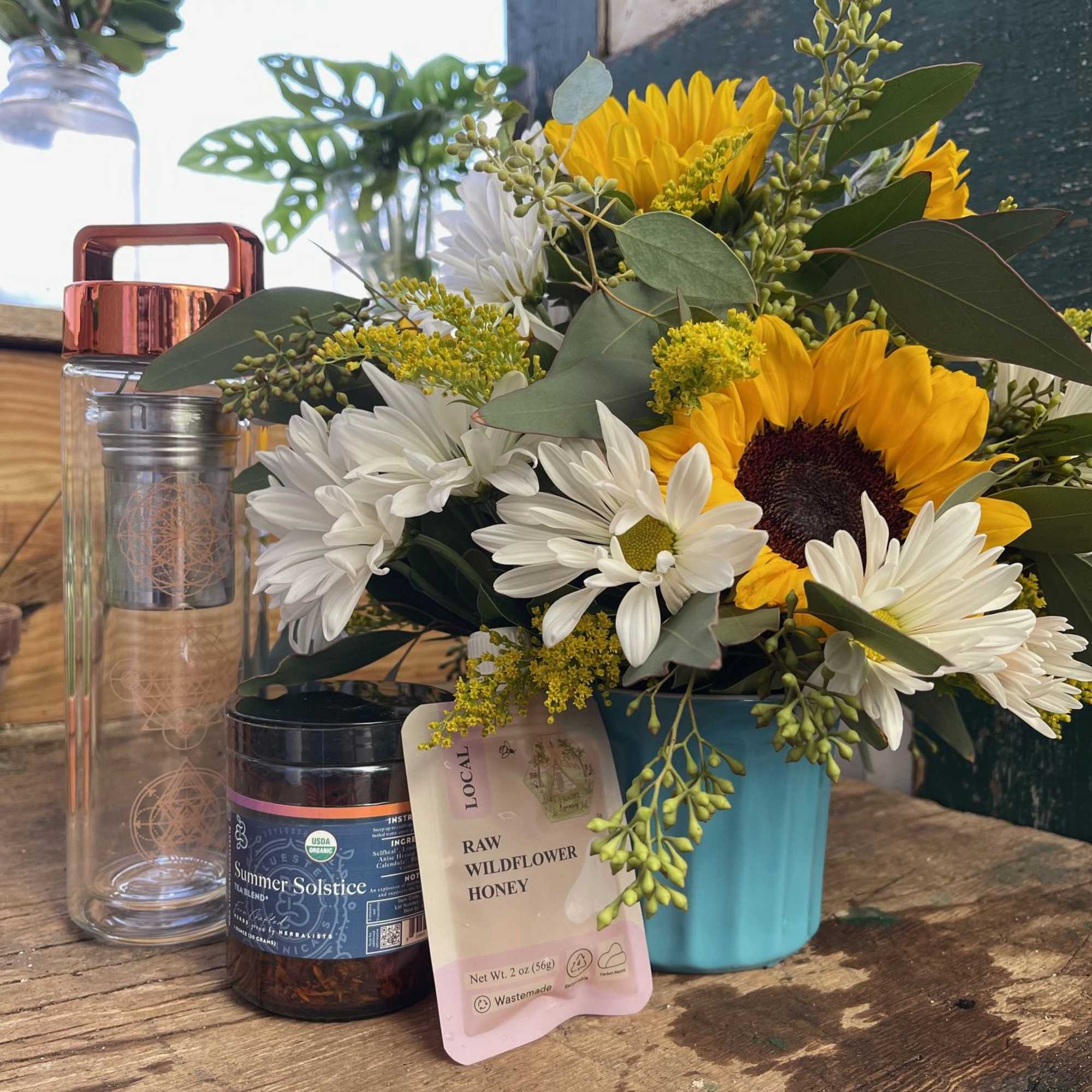 Sunflower and white daisy bouquet in a blue container with honey and a jar beside it