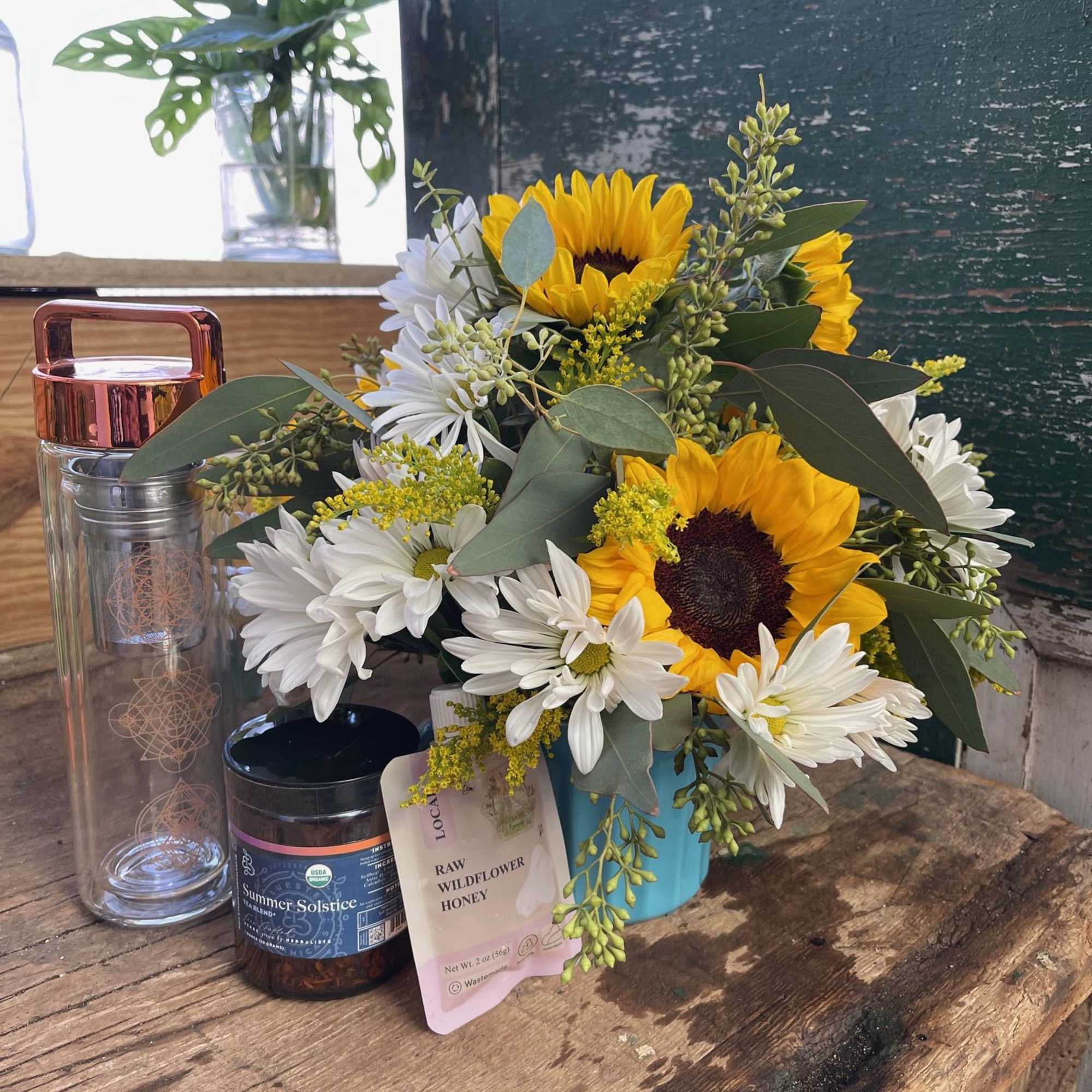 Sunflower and white daisy bouquet in a blue container with honey and a bottle