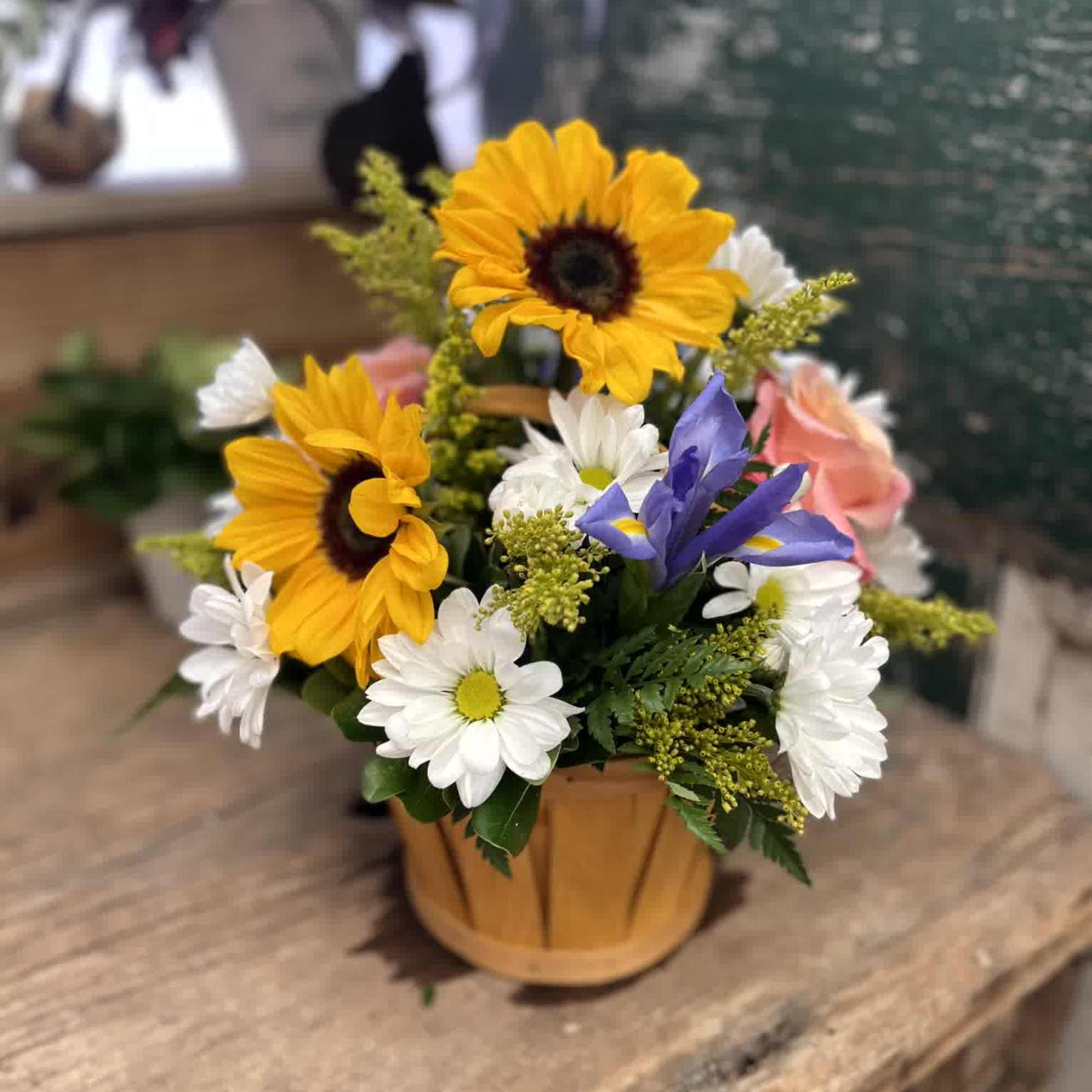 Mixed bouquet in a small wooden basket with sunflowers, daisies, and a purple iris